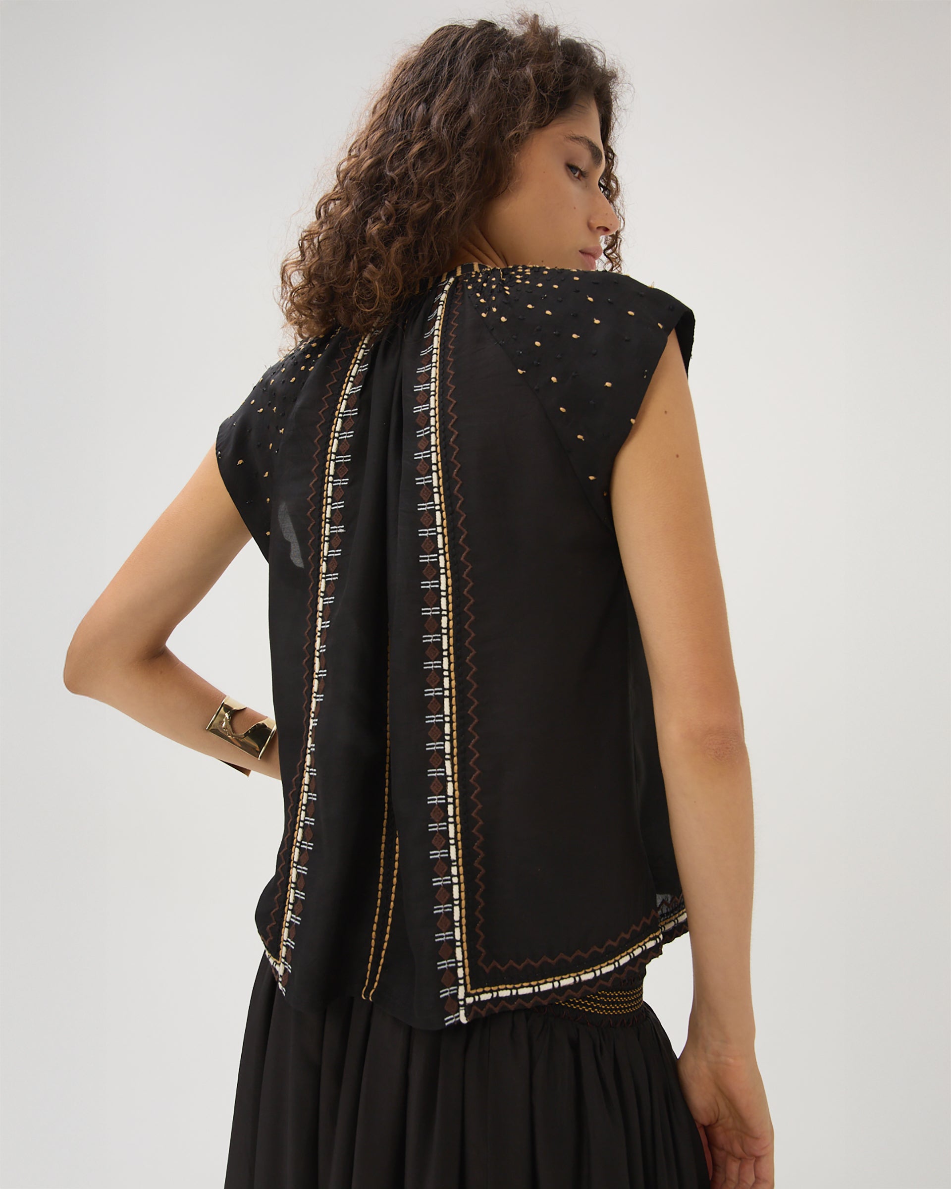 Woman wearing a black sleeveless top with intricate gold detailing on a white background
