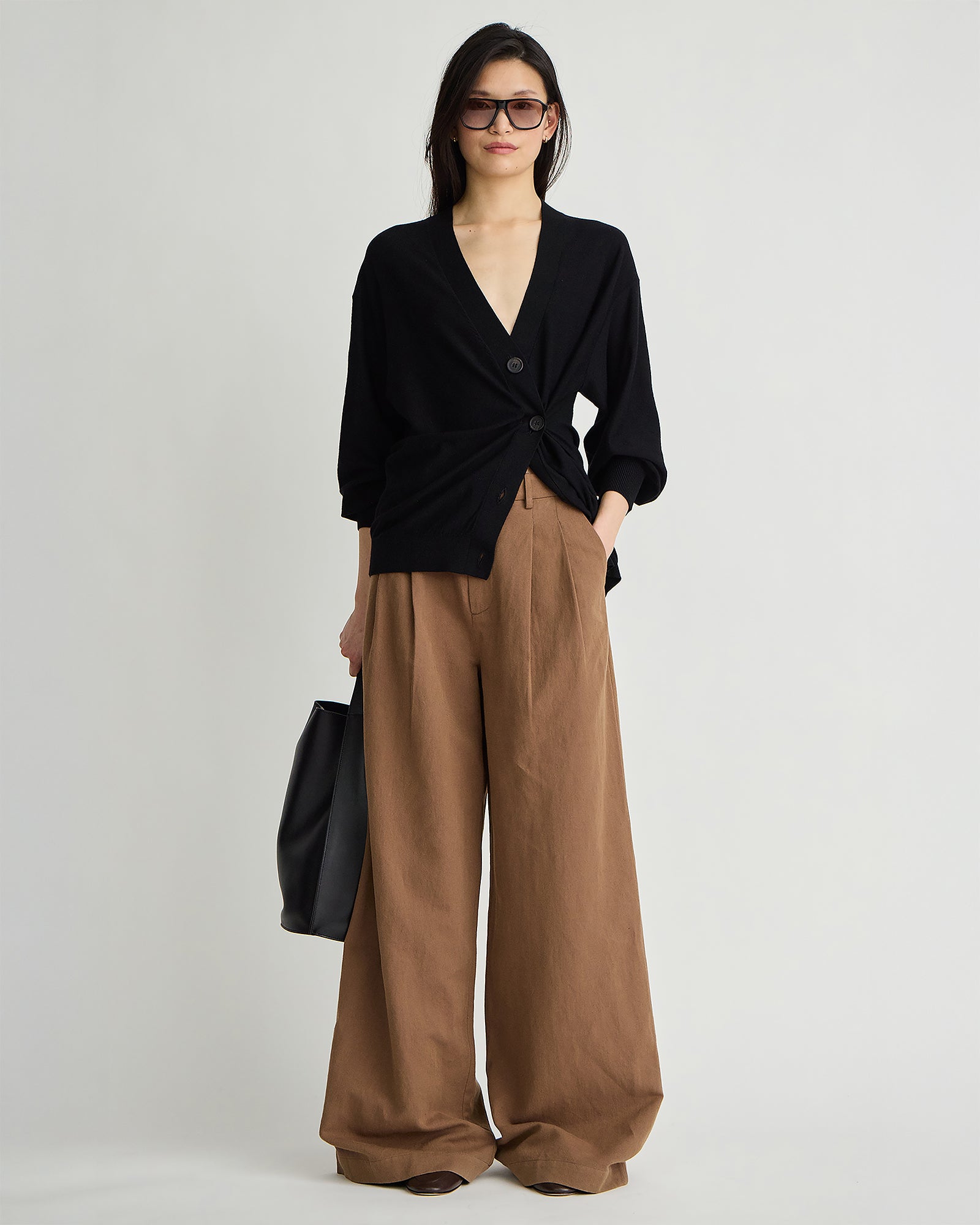 model wearing tobacco pleated pants and a black cardigan and sunglasses