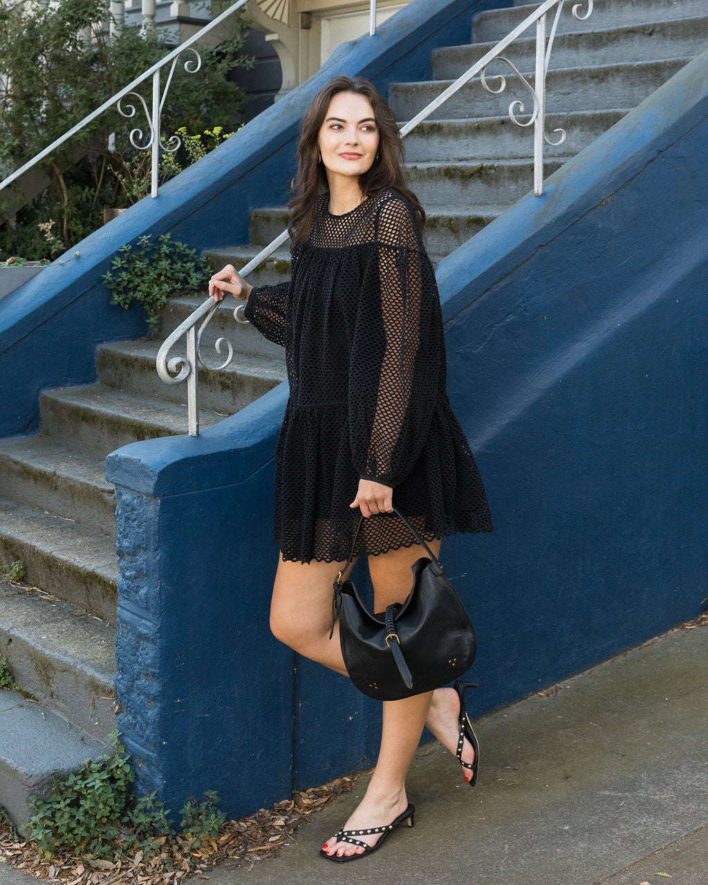 Woman in a black dress standing on a staircase with a blue wall.