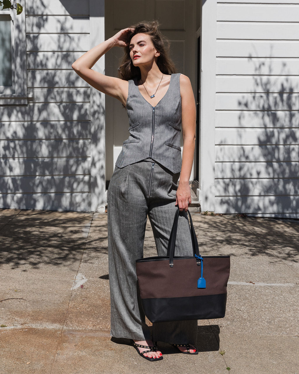 Woman in a gray jumpsuit holding a black tote bag outdoors.