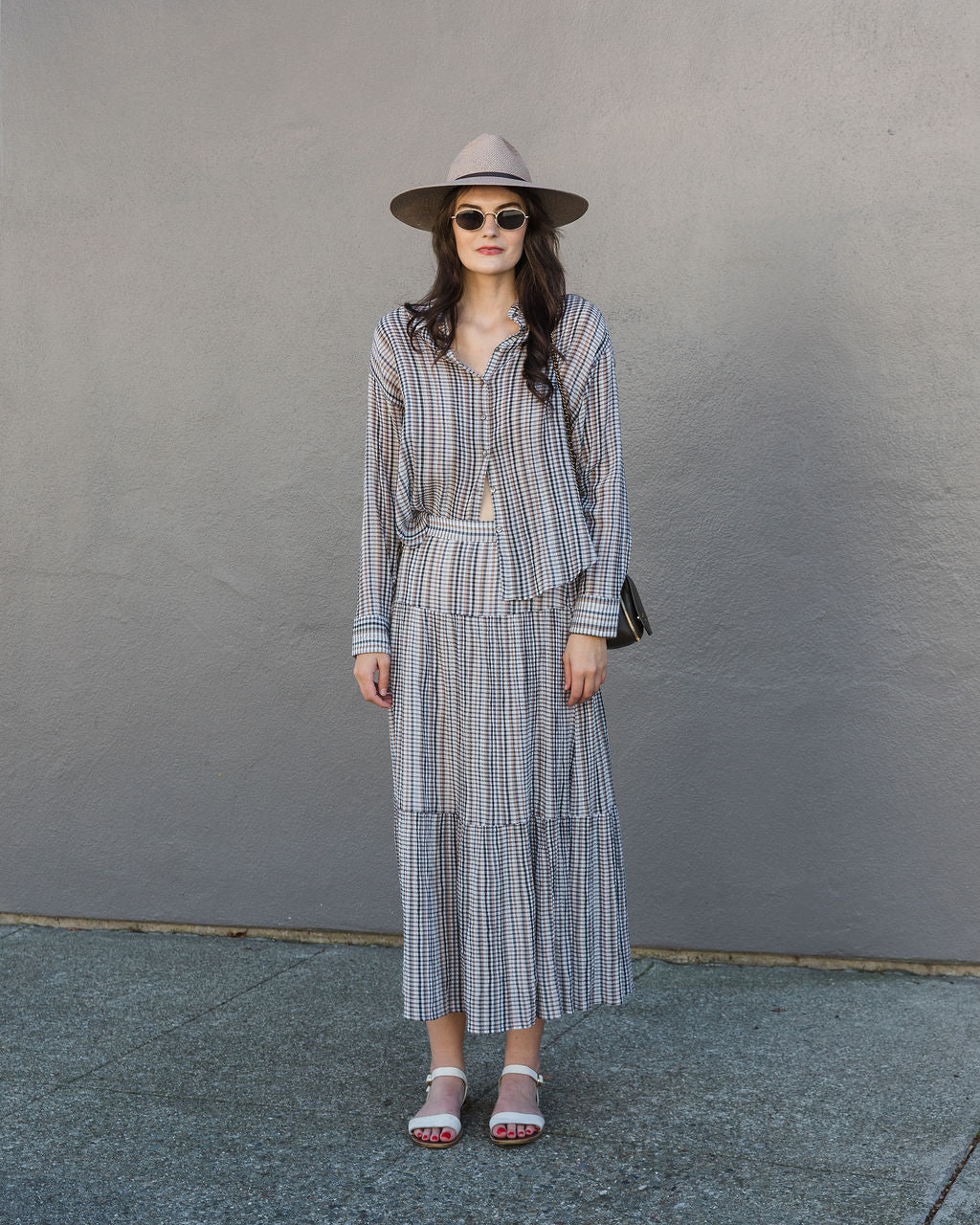 Woman wearing a checkered outfit with a hat against a gray wall.