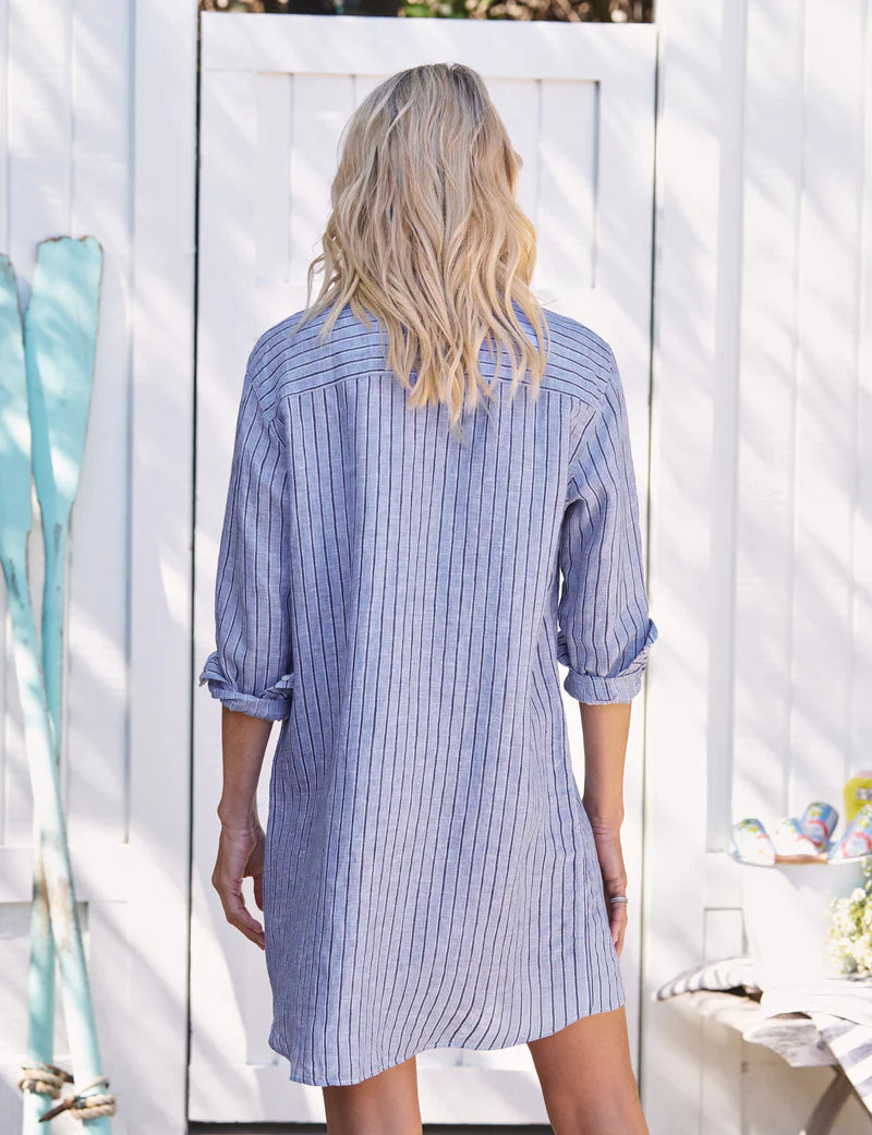 Woman wearing a blue striped shirt dress standing in a bright outdoor setting.
