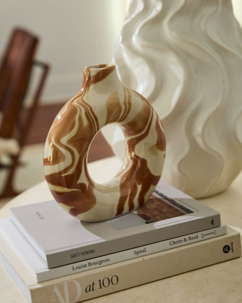 Decorative vase on top of books with a wavy-patterned vase in the background