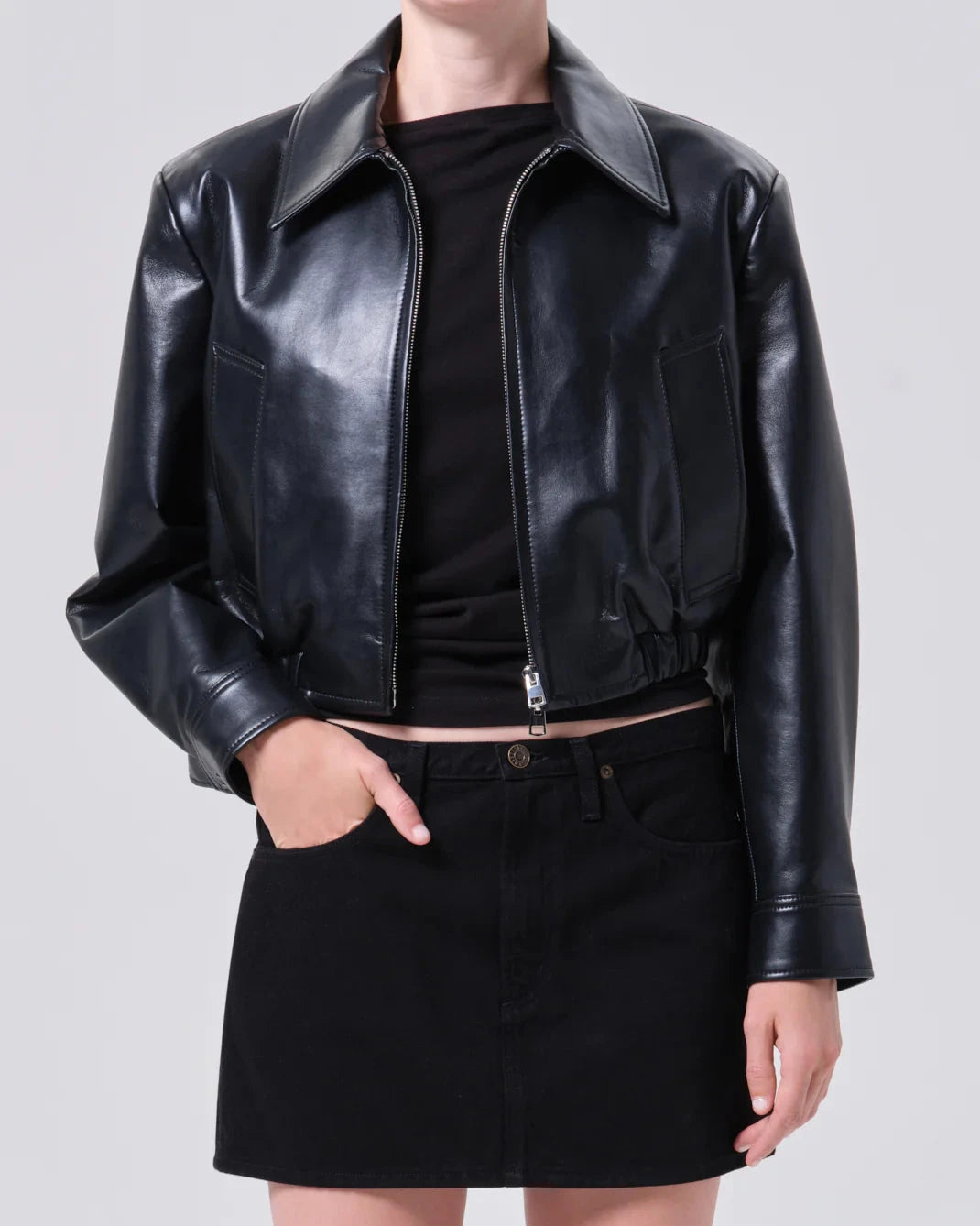 Person wearing a black leather jacket over a black top and skirt on a light gray background