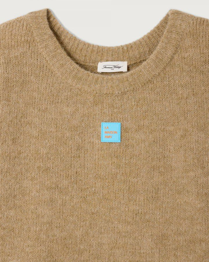 Beige sweater with a blue patch and brand label on a light gray background