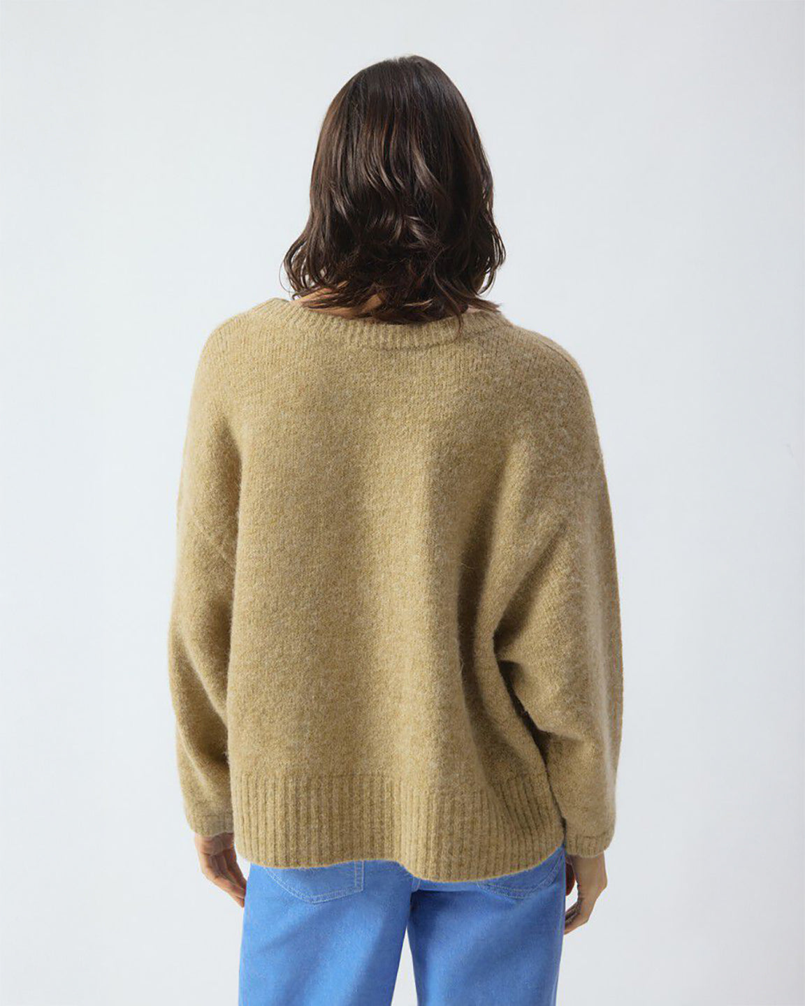 Person wearing a beige sweater and blue pants against a white background