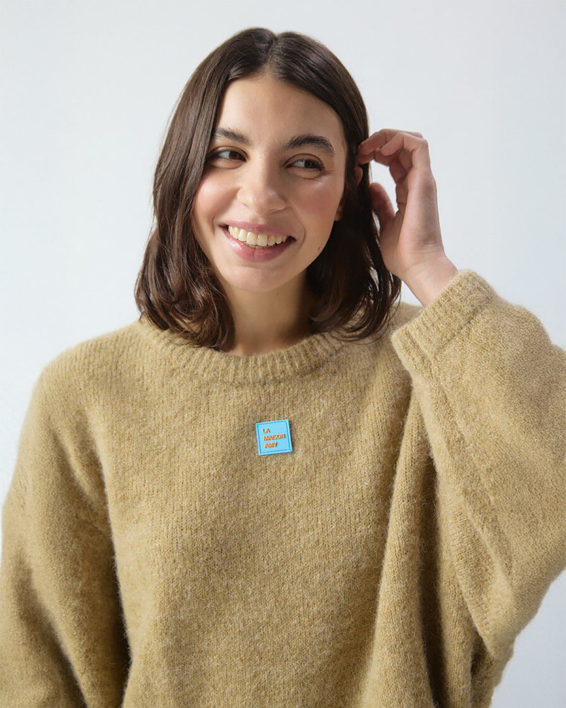 Woman wearing a beige sweater with a blue tag on a light gray background