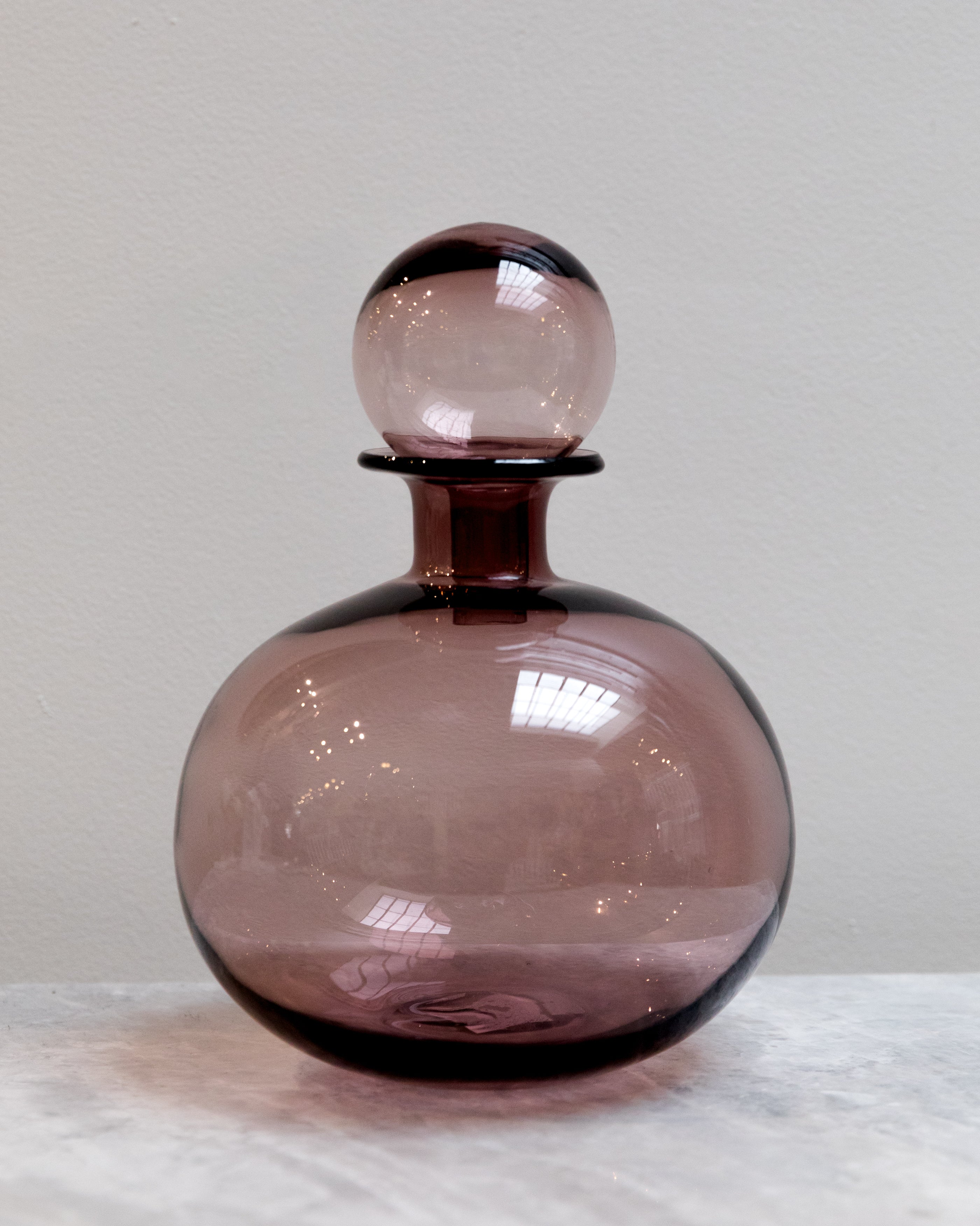 Purple glass decanter with a spherical stopper on a white surface.