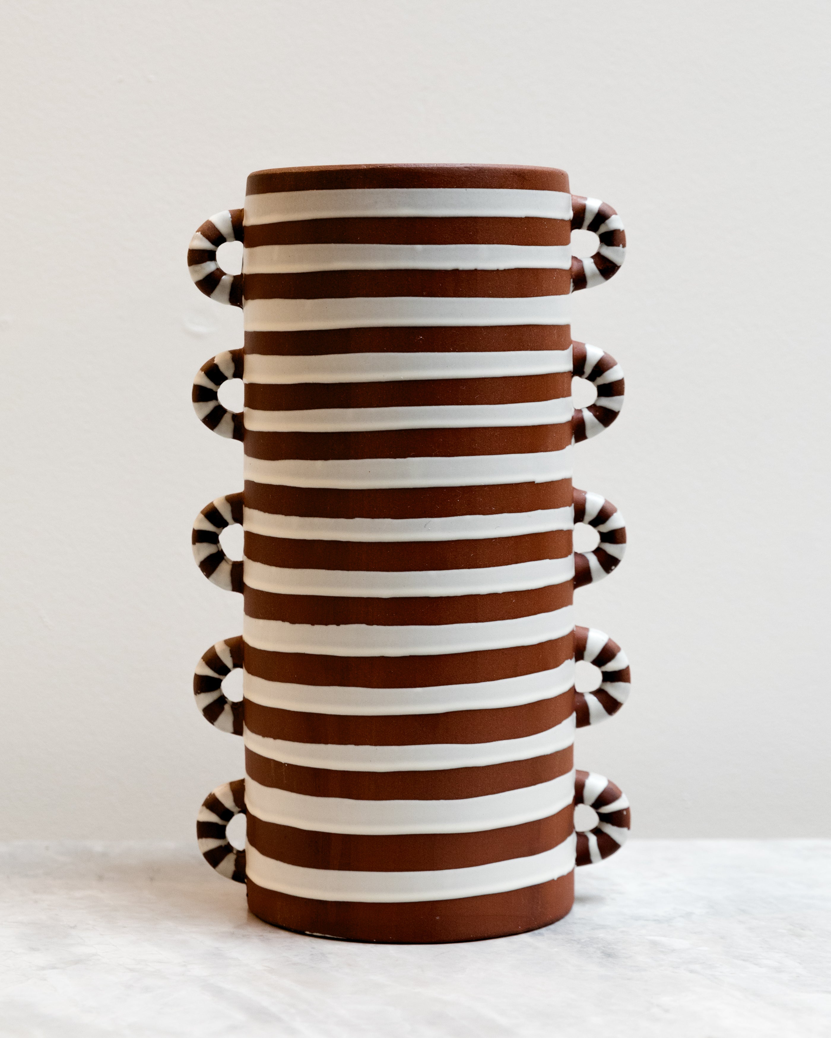 Decorative vase with brown and white striped pattern and pom-pom details on a light background