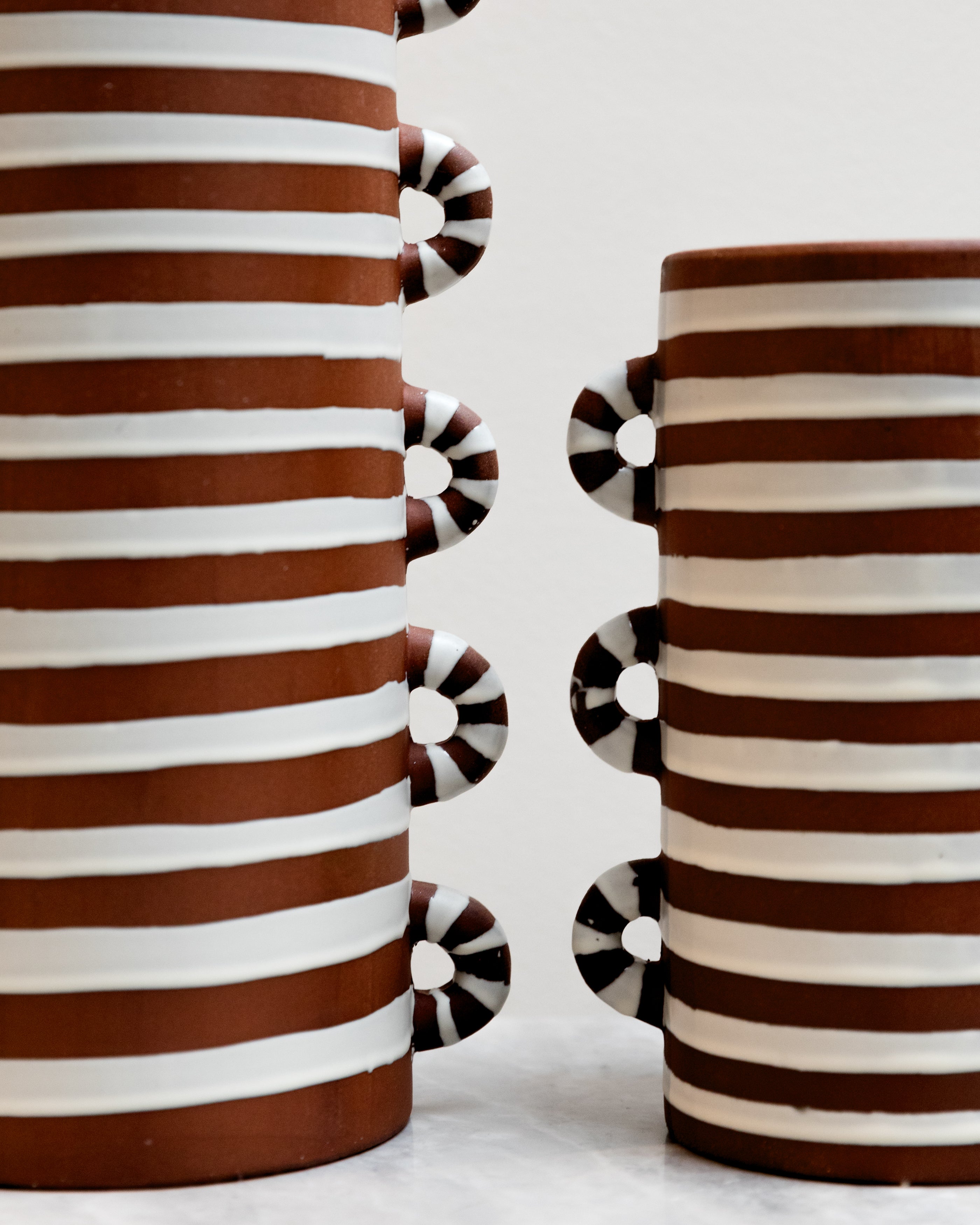 Two ceramic vases with brown and white striped design on a light background