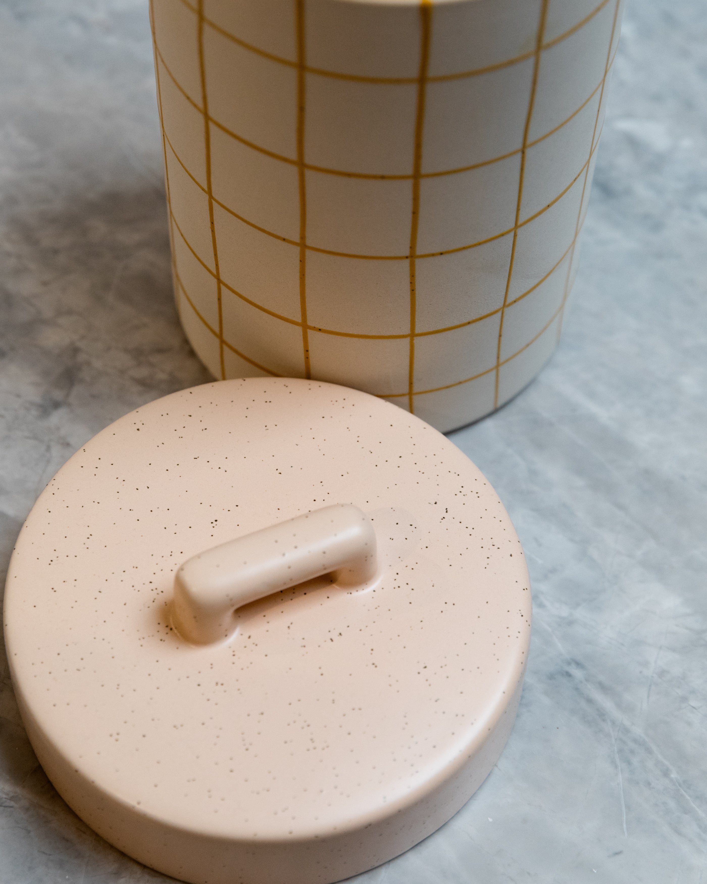 Ceramic container with grid-patterned lid on a textured surface