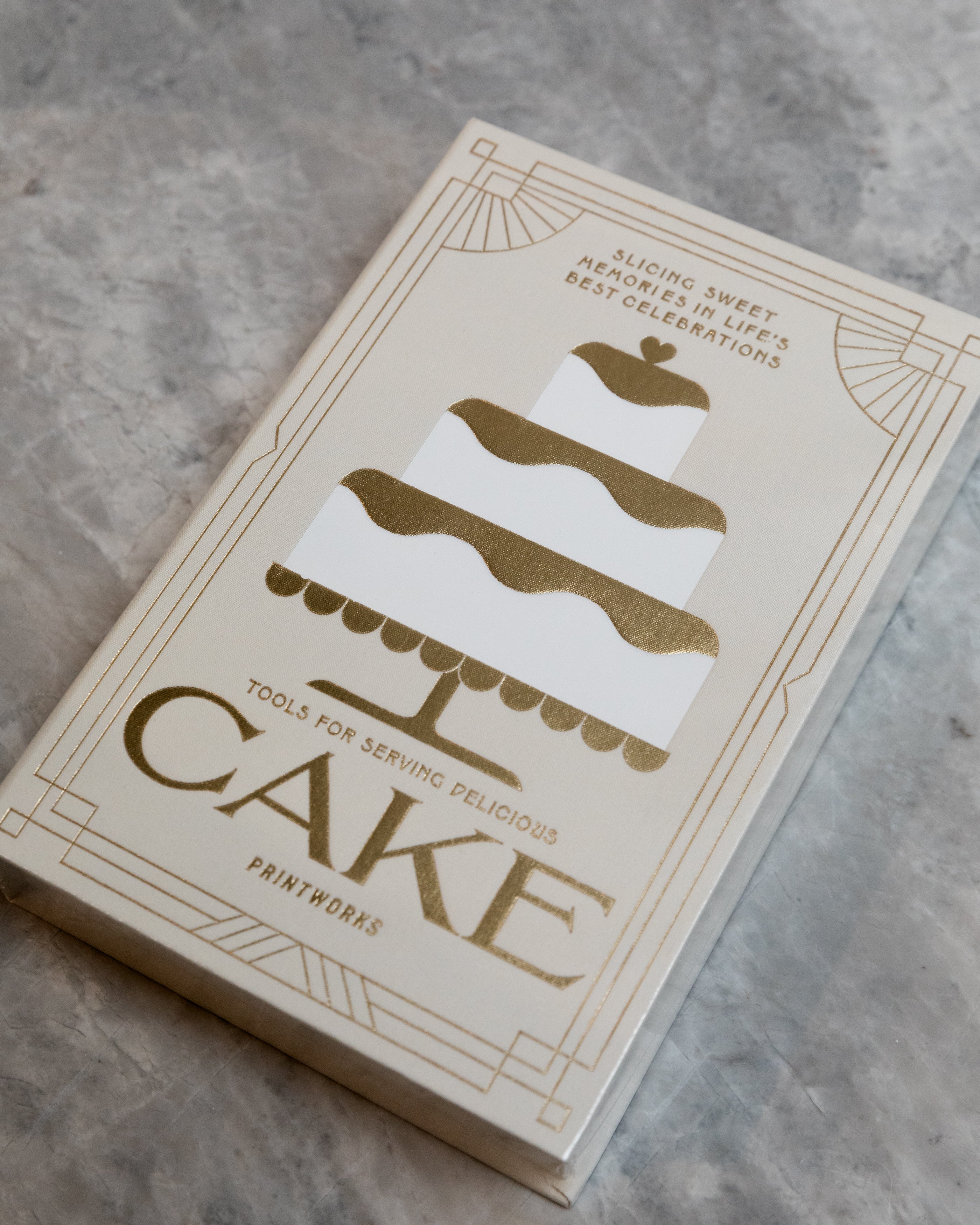 3 tiered white cake with gold frosting printed on a box that also tools for serving cake