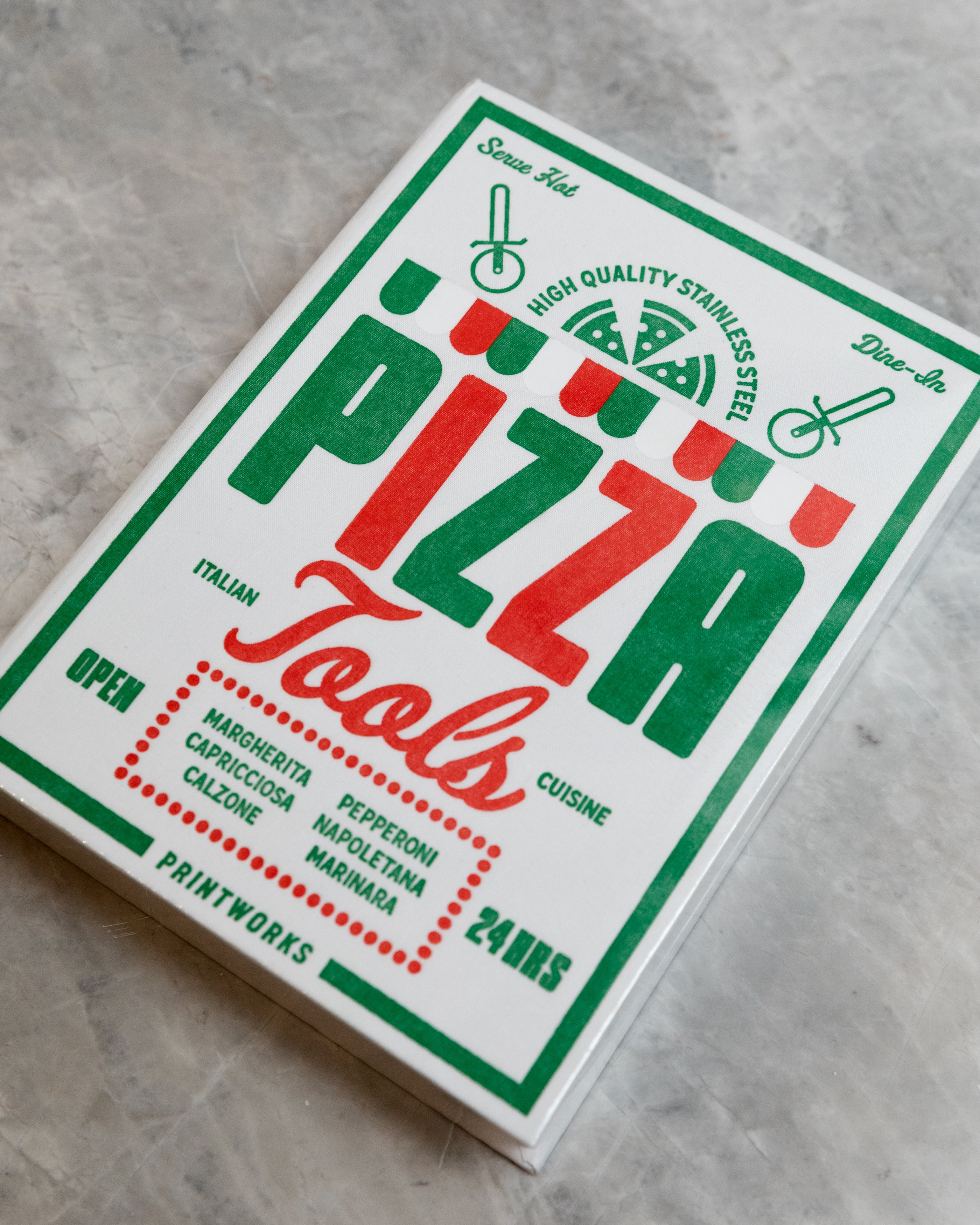 Box of pizza tools with red and green text on a gray surface