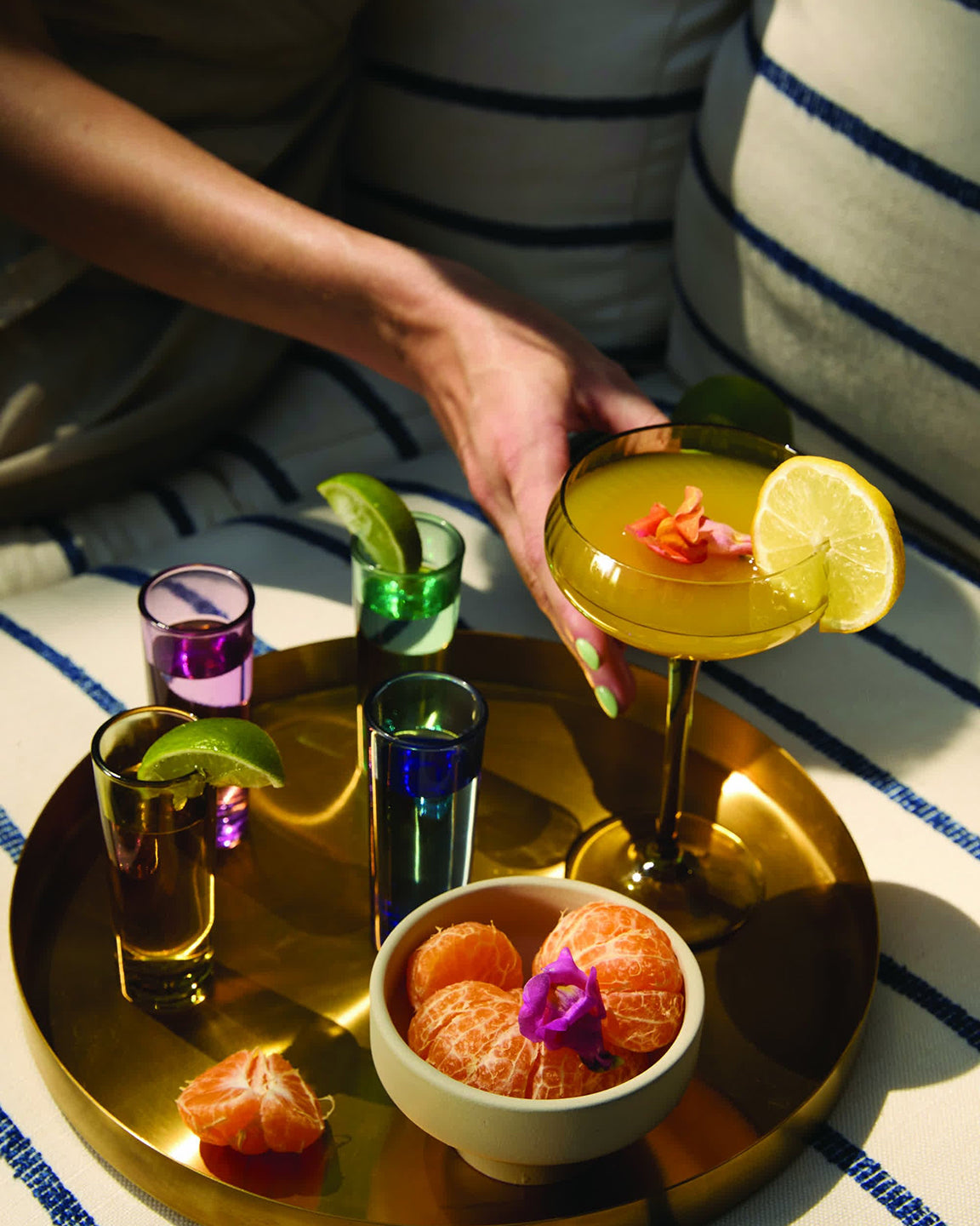 Cocktail with garnish on a gold tray with other drinks and fruit