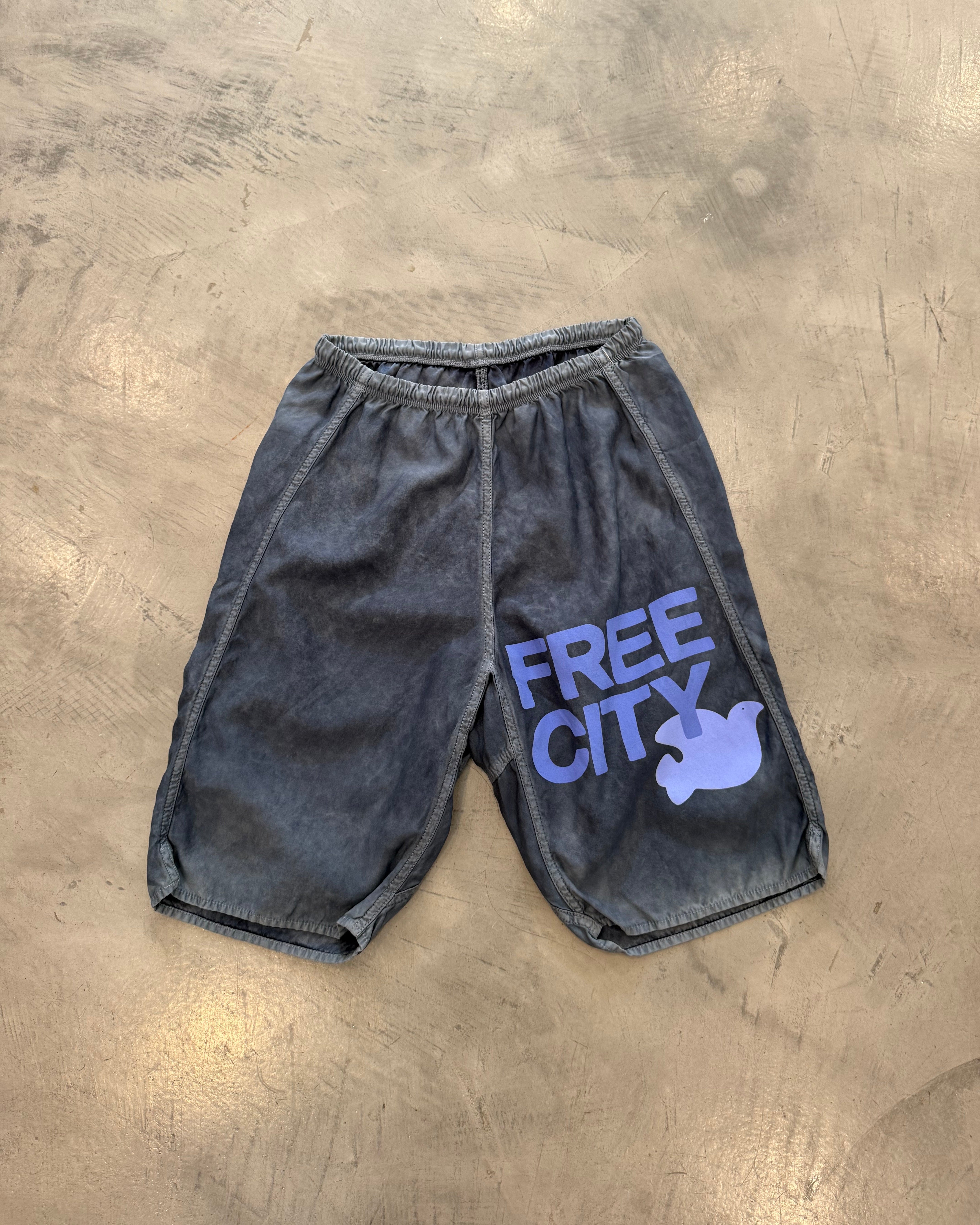 Black knee shorts with 'Free City' logo on a concrete surface