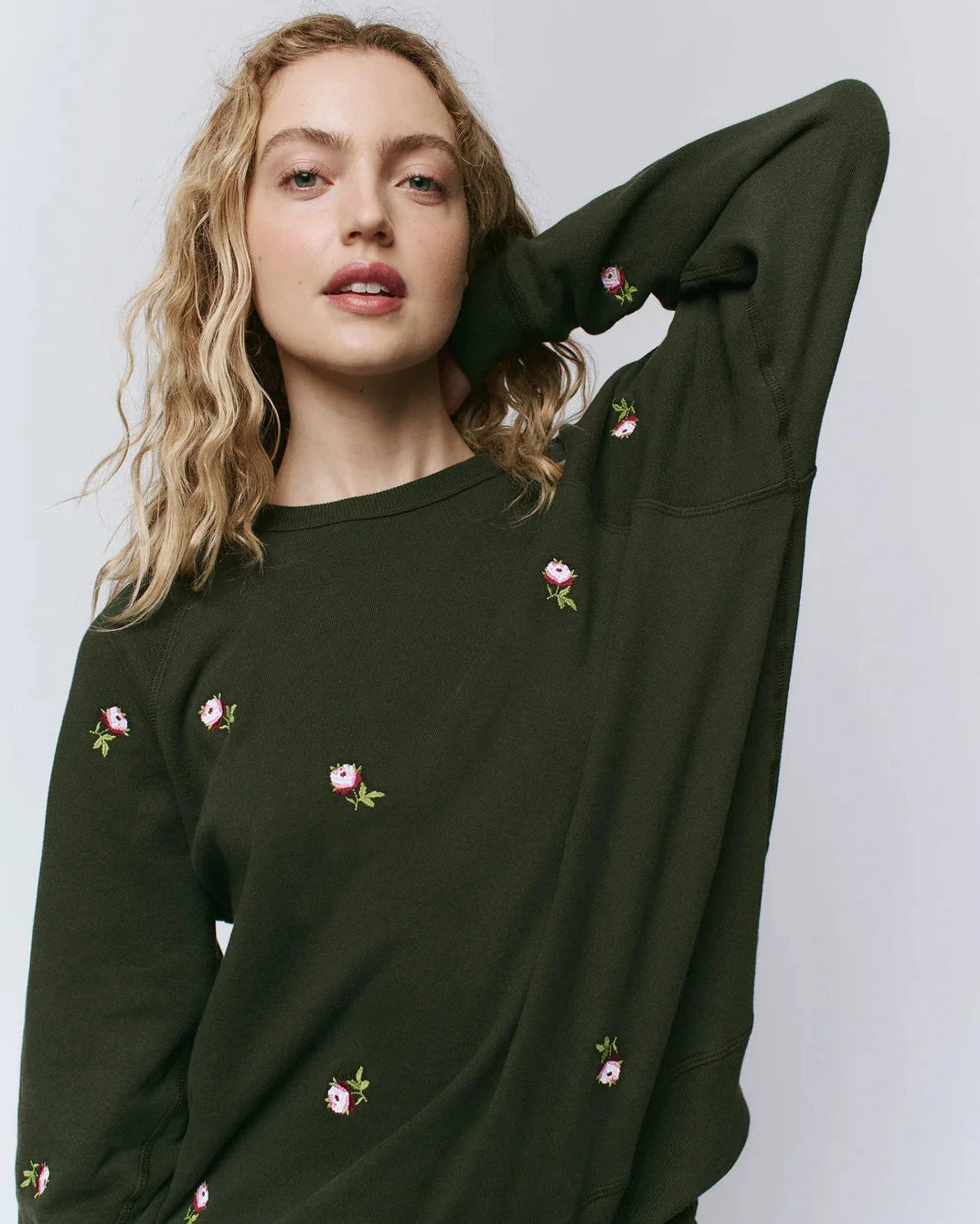 Woman wearing a dark green sweatshirt with floral embroidery on a plain background