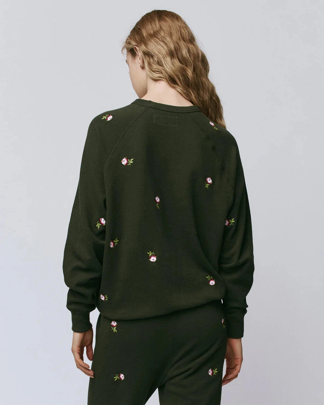 Person wearing a black sweatshirt with floral embroidery on a plain background