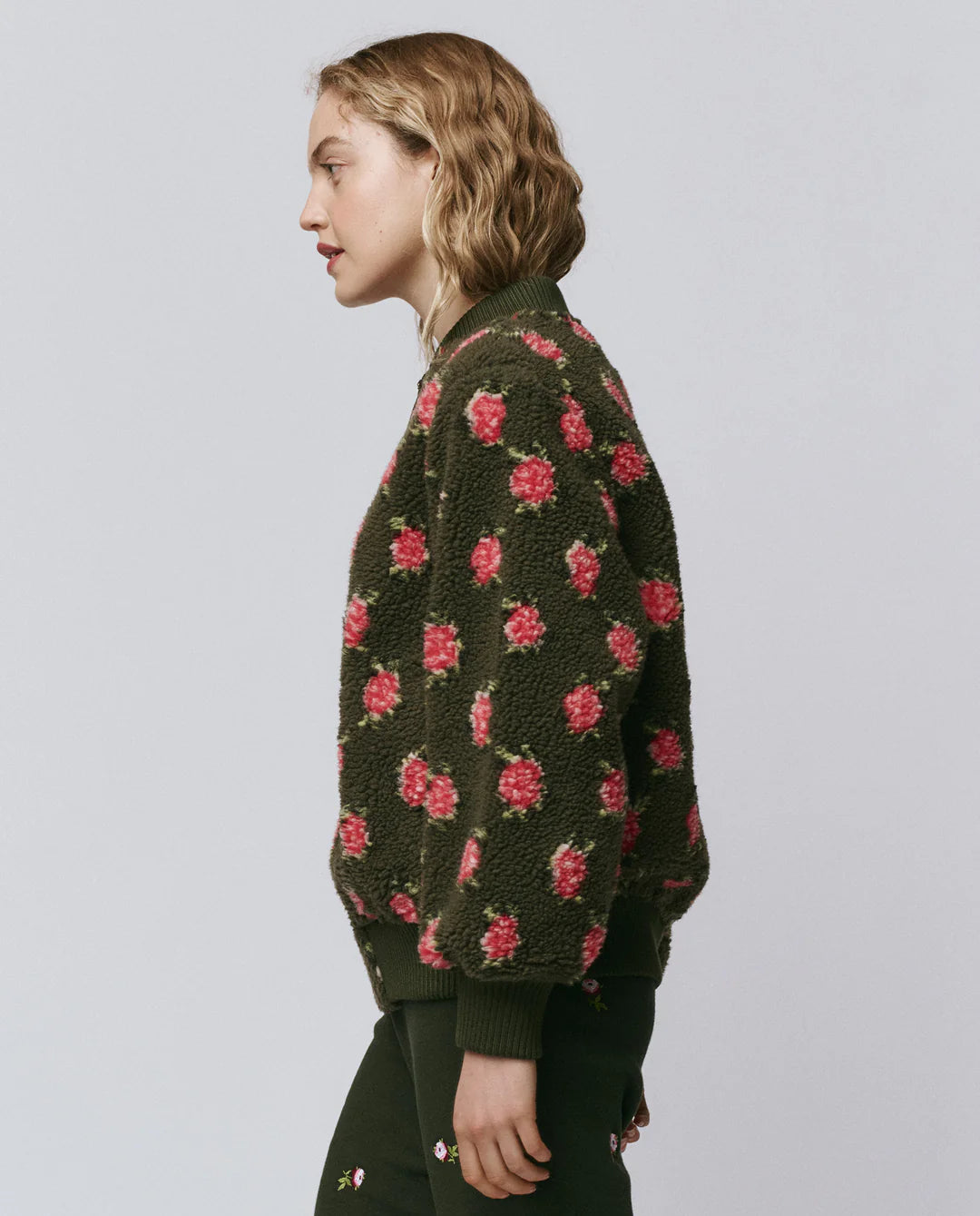 Person wearing a dark green bomber jacket with red floral patterns on a plain background