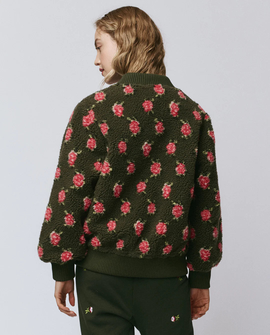 Person wearing a dark green sweater with pink floral patterns on a plain background