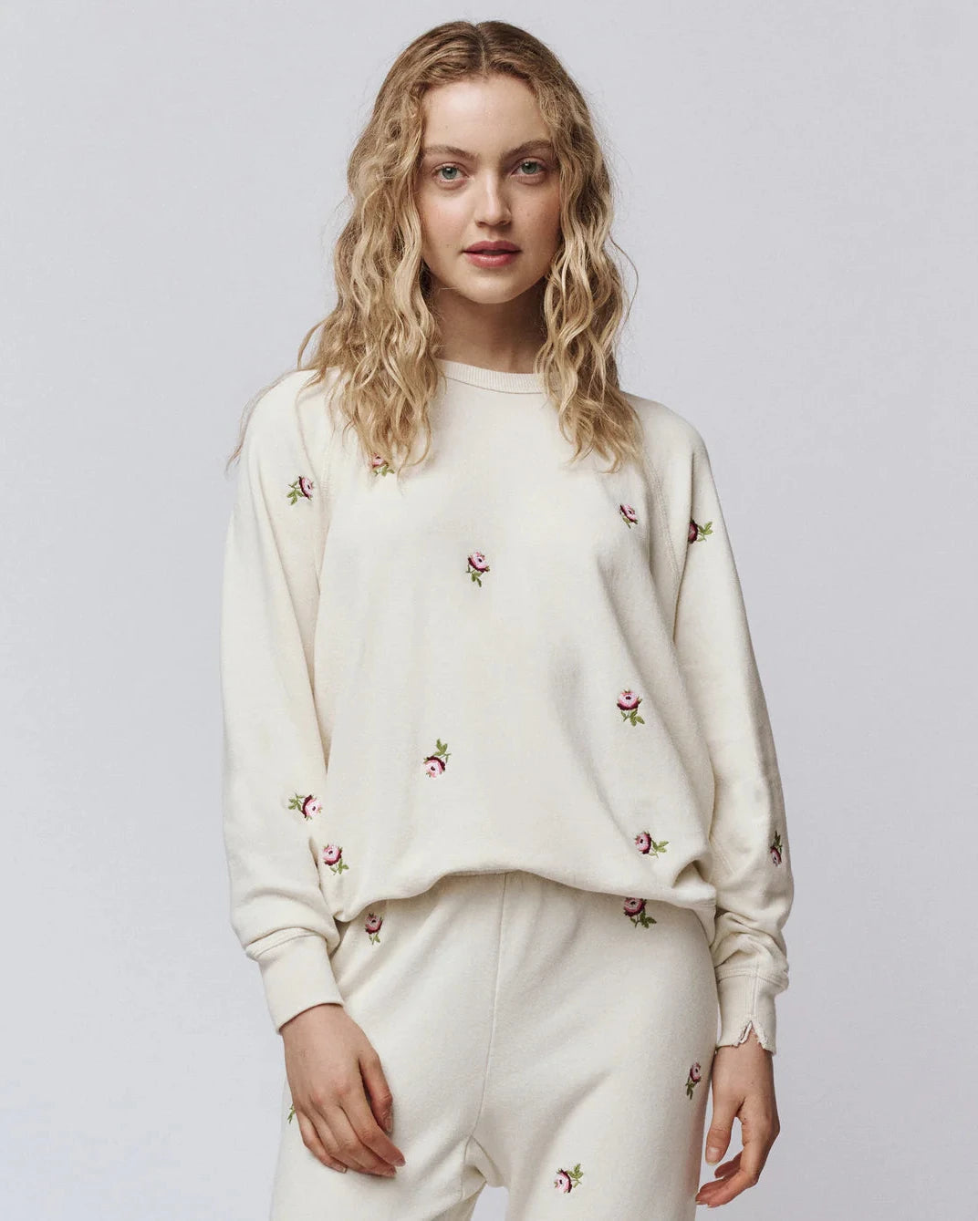 Woman wearing a cream-colored sweatshirt with floral embroidery on a plain background