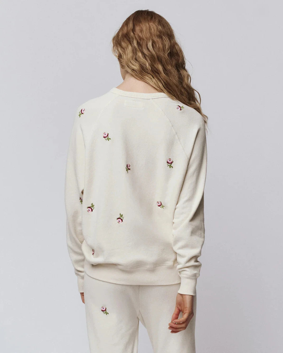 Person wearing a cream-colored sweatshirt with floral embroidery on a plain background