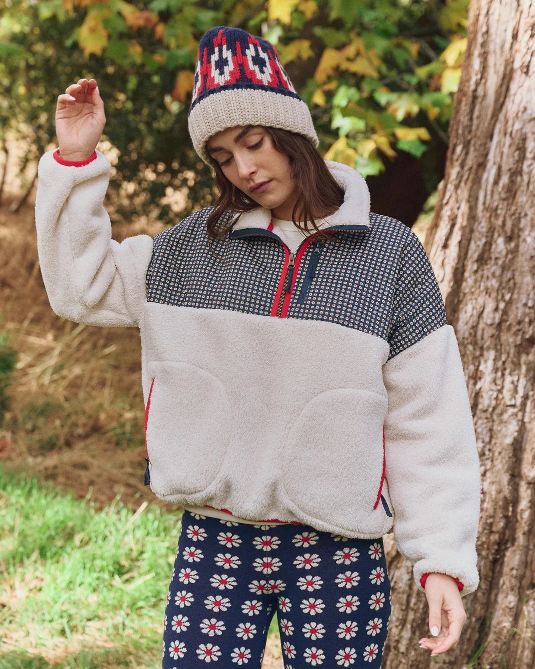 Person wearing a patterned beanie, checkered jacket, and floral pants in a forest setting