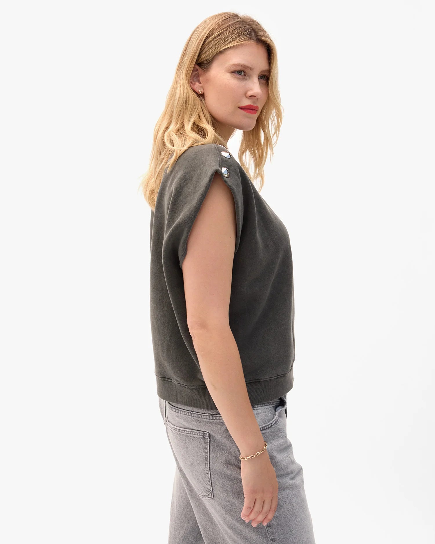 Woman wearing a dark green sleeveless top and light gray pants on a white background