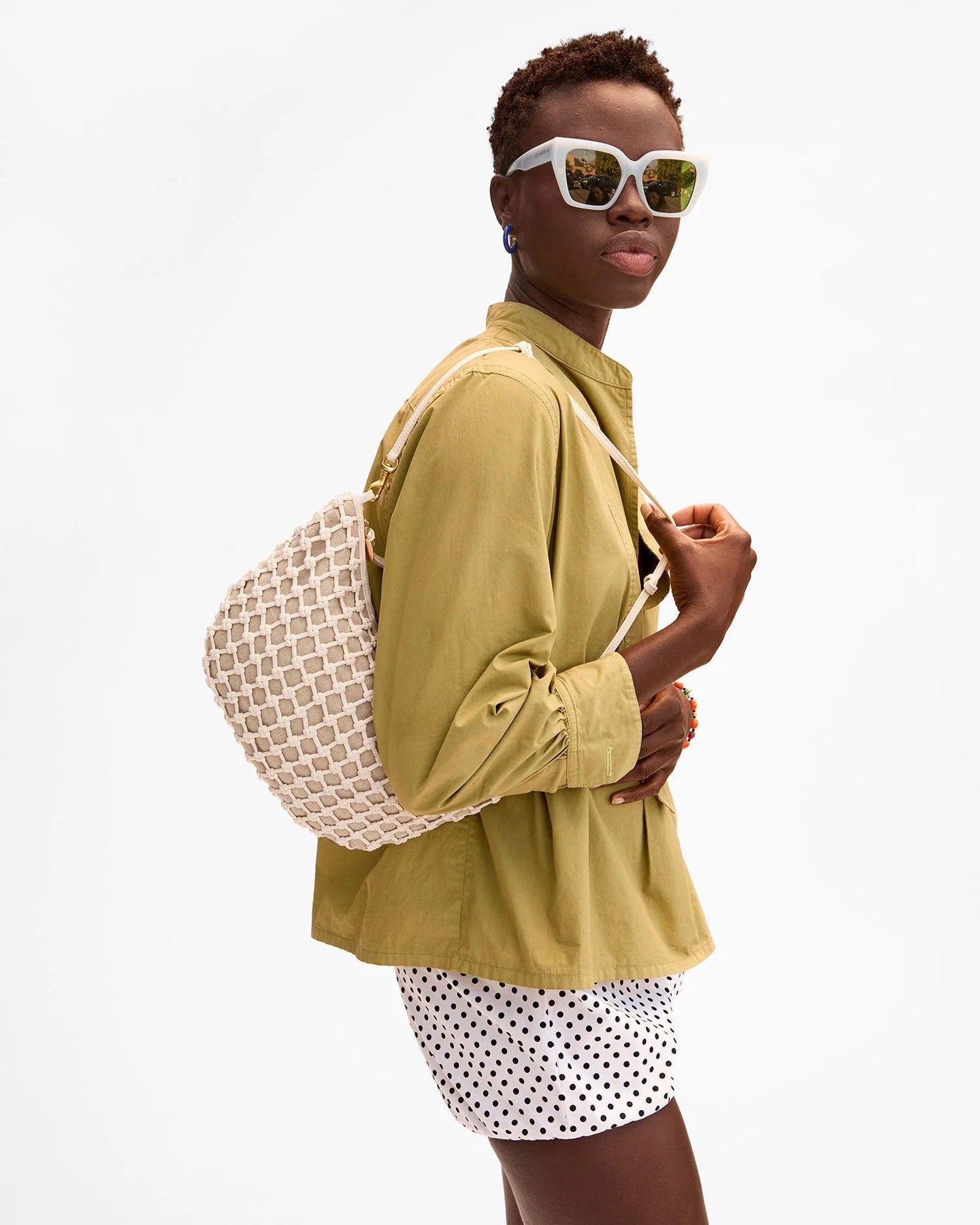 Person wearing a green jacket and polka dot shorts with a patterned bag on a white background