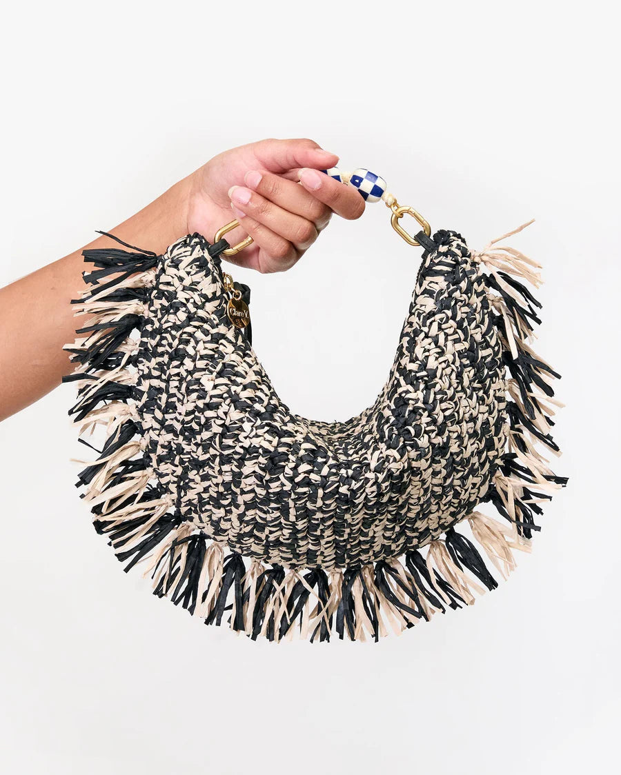 Hand holding a black and beige woven necklace with tassels on a white background