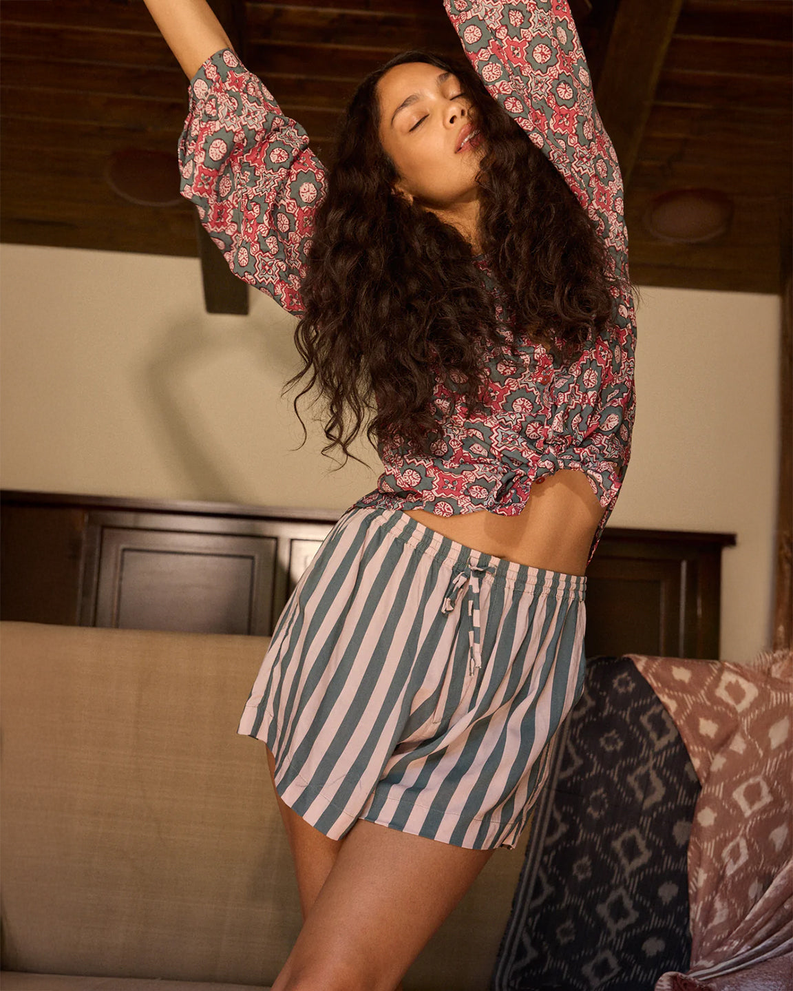 Woman in a floral top and striped shorts posing in a room.
