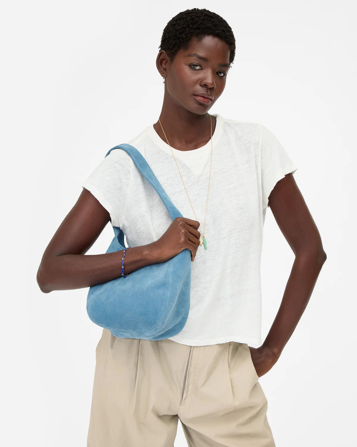 Person wearing a white shirt and beige pants with a blue bag on a white background