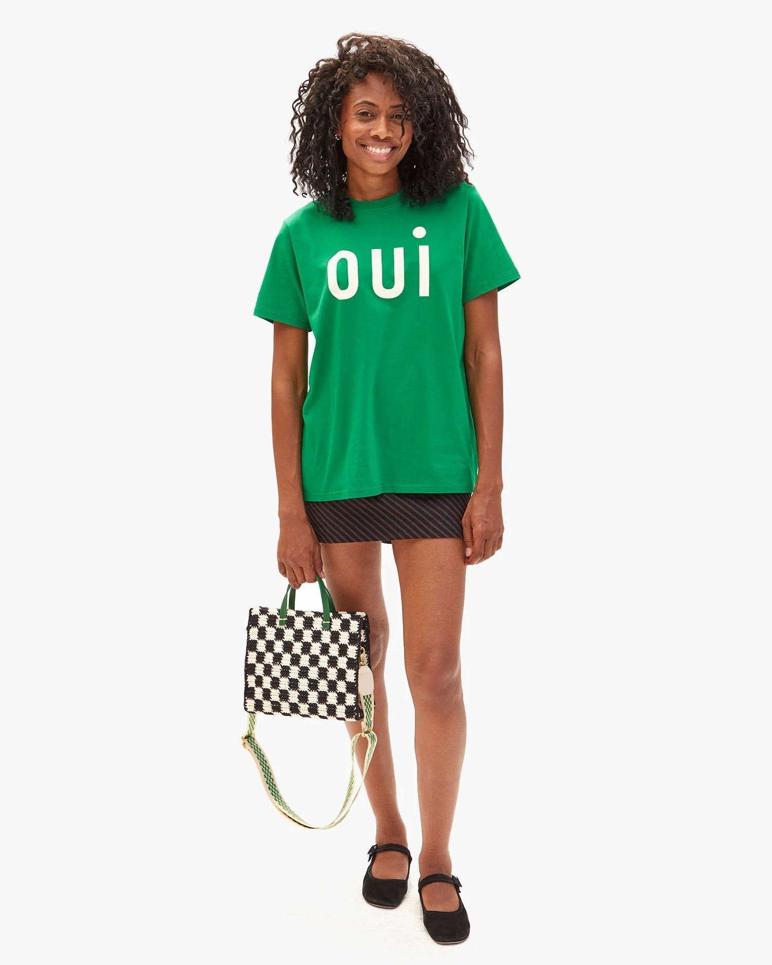 Person wearing a green 'OUI' t-shirt holding a checkered bag on a white background