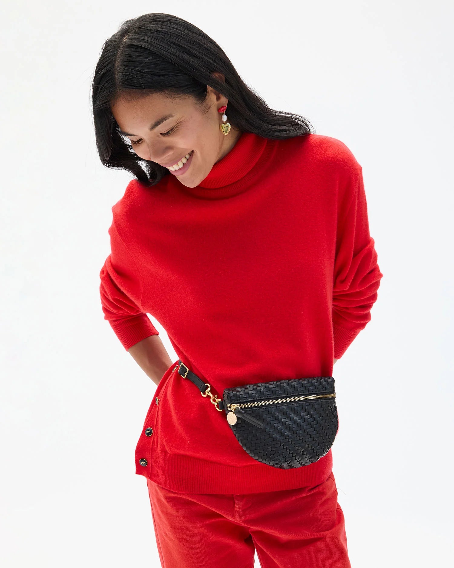 Woman wearing a red sweater and red pants with a black fanny pack on a white background