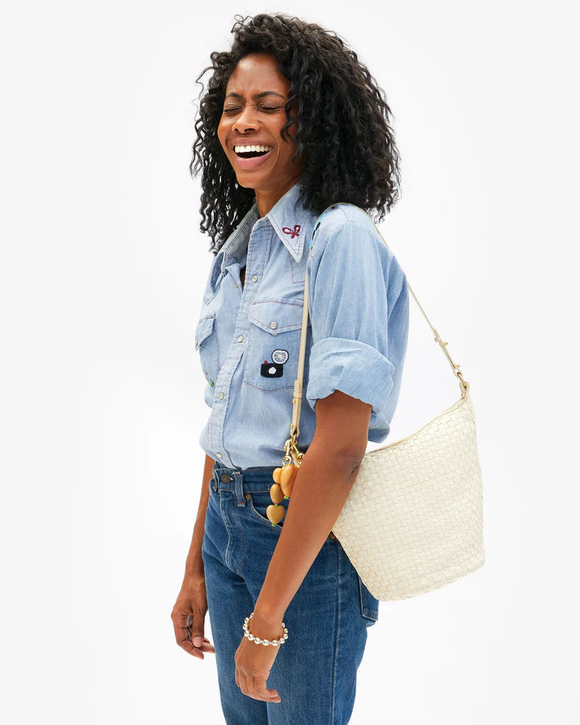 Woman wearing a denim shirt and jeans, holding a white handbag on a white background