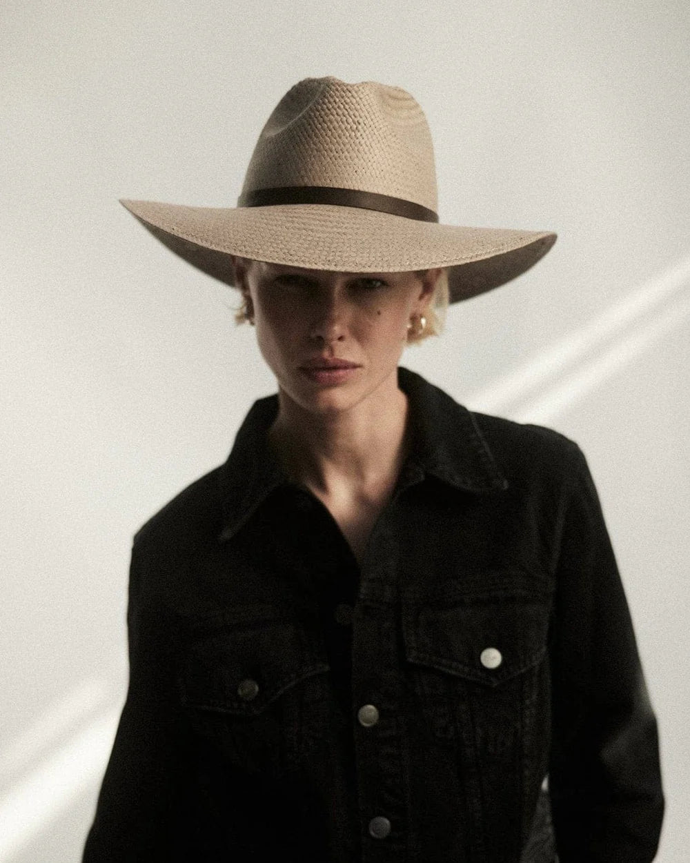 Person wearing a wide-brimmed hat and dark jacket against a white background