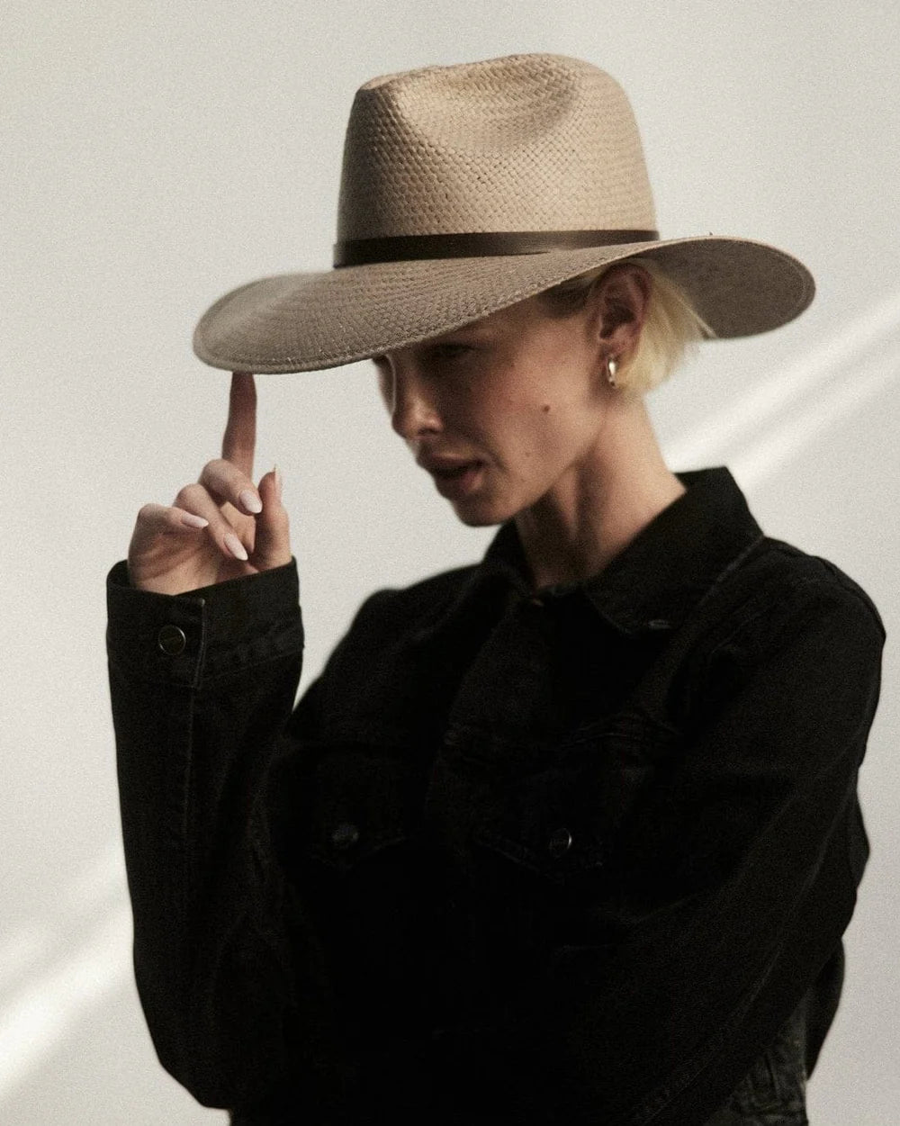 Person wearing a wide-brimmed hat and black shirt against a neutral background