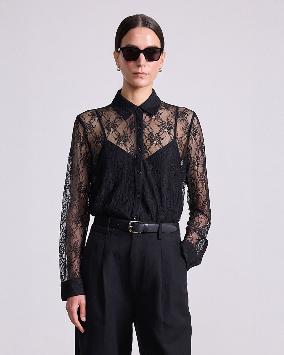 Person wearing a black lace blouse and black pants on a light gray background