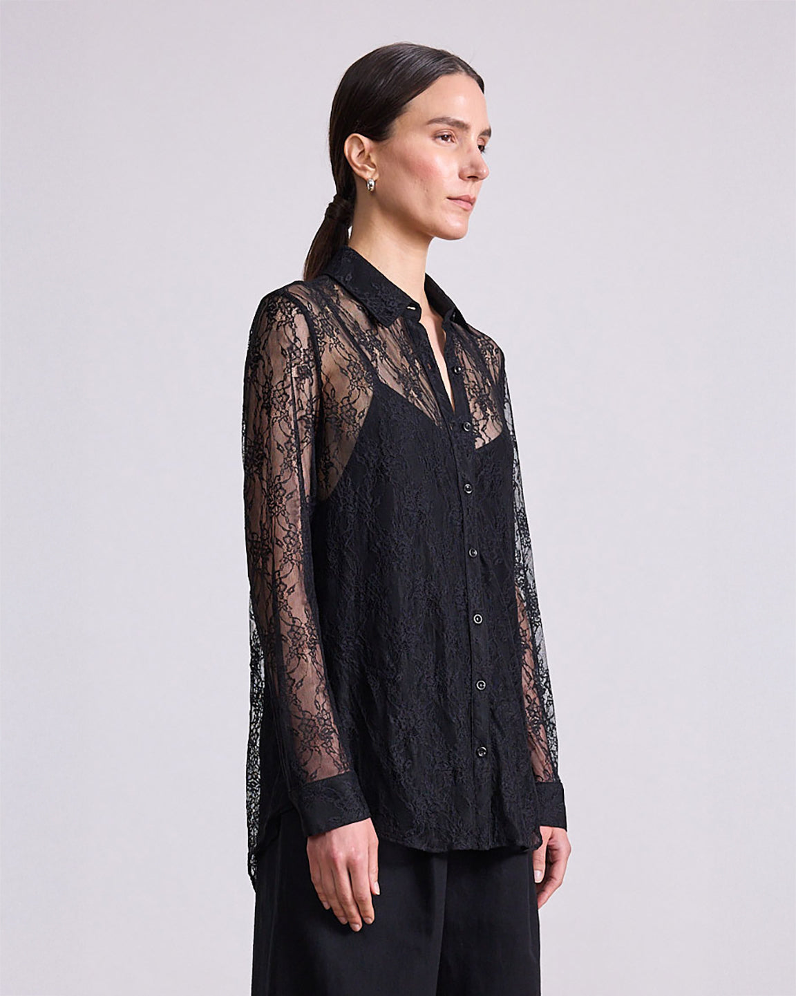 Woman wearing a black lace shirt against a plain background