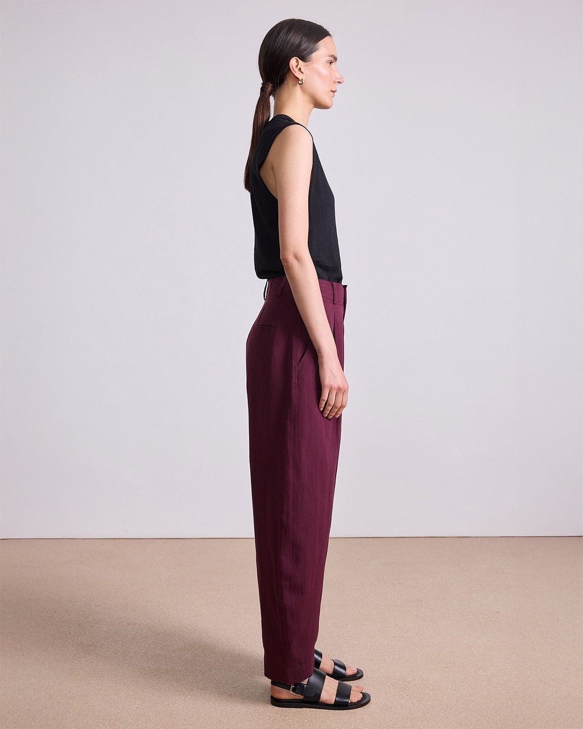 Woman wearing a black sleeveless top and burgundy pants against a plain background