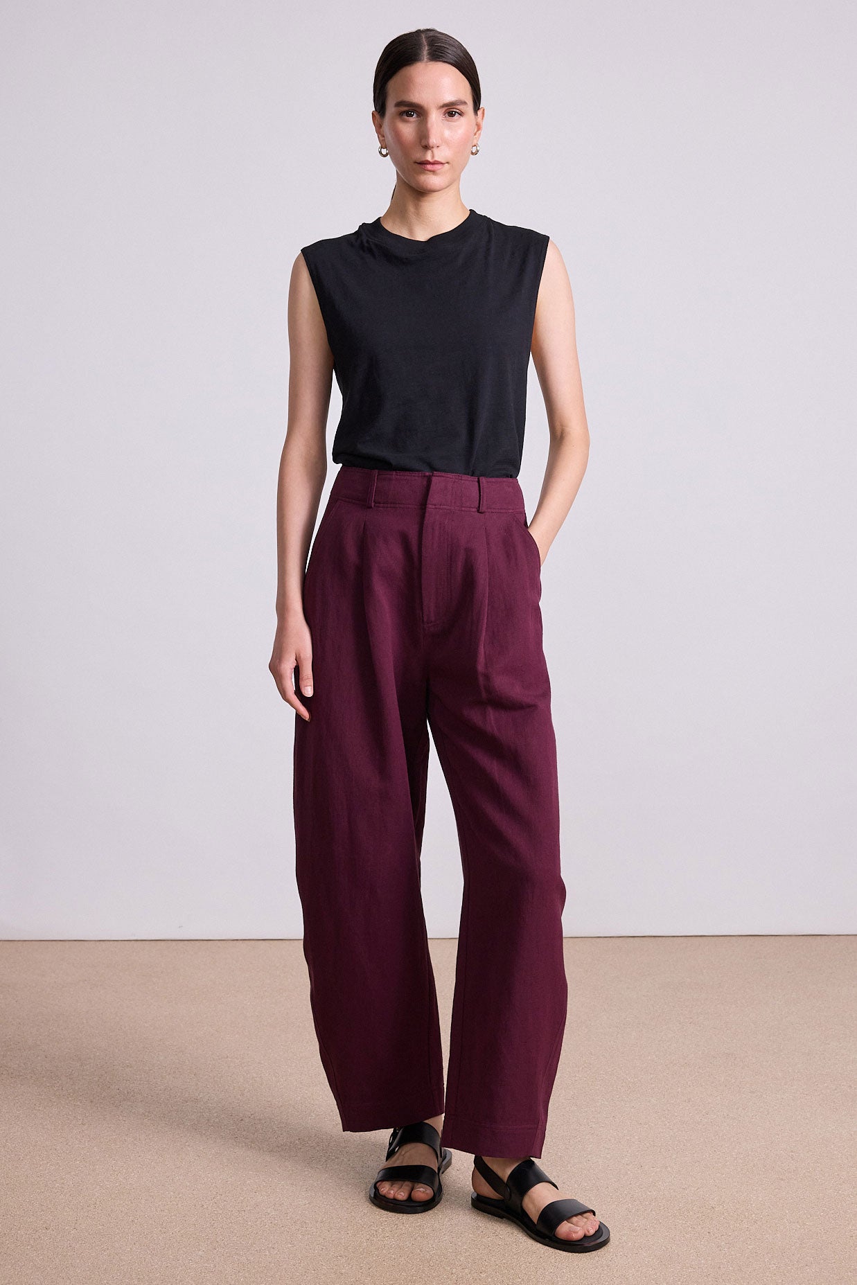 Woman wearing a black sleeveless top and burgundy pants on a plain background
