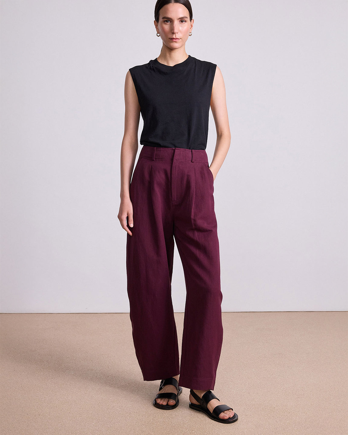 Woman wearing a black sleeveless top and maroon pants on a plain background