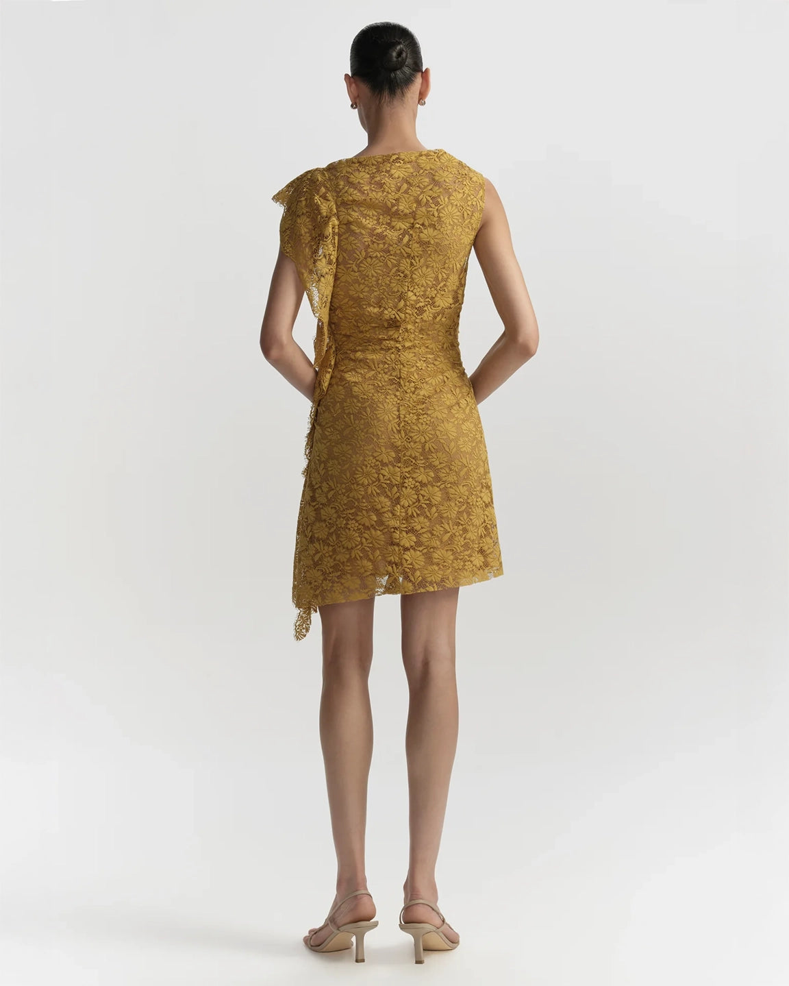 Woman wearing a mustard yellow lace dress on a white background