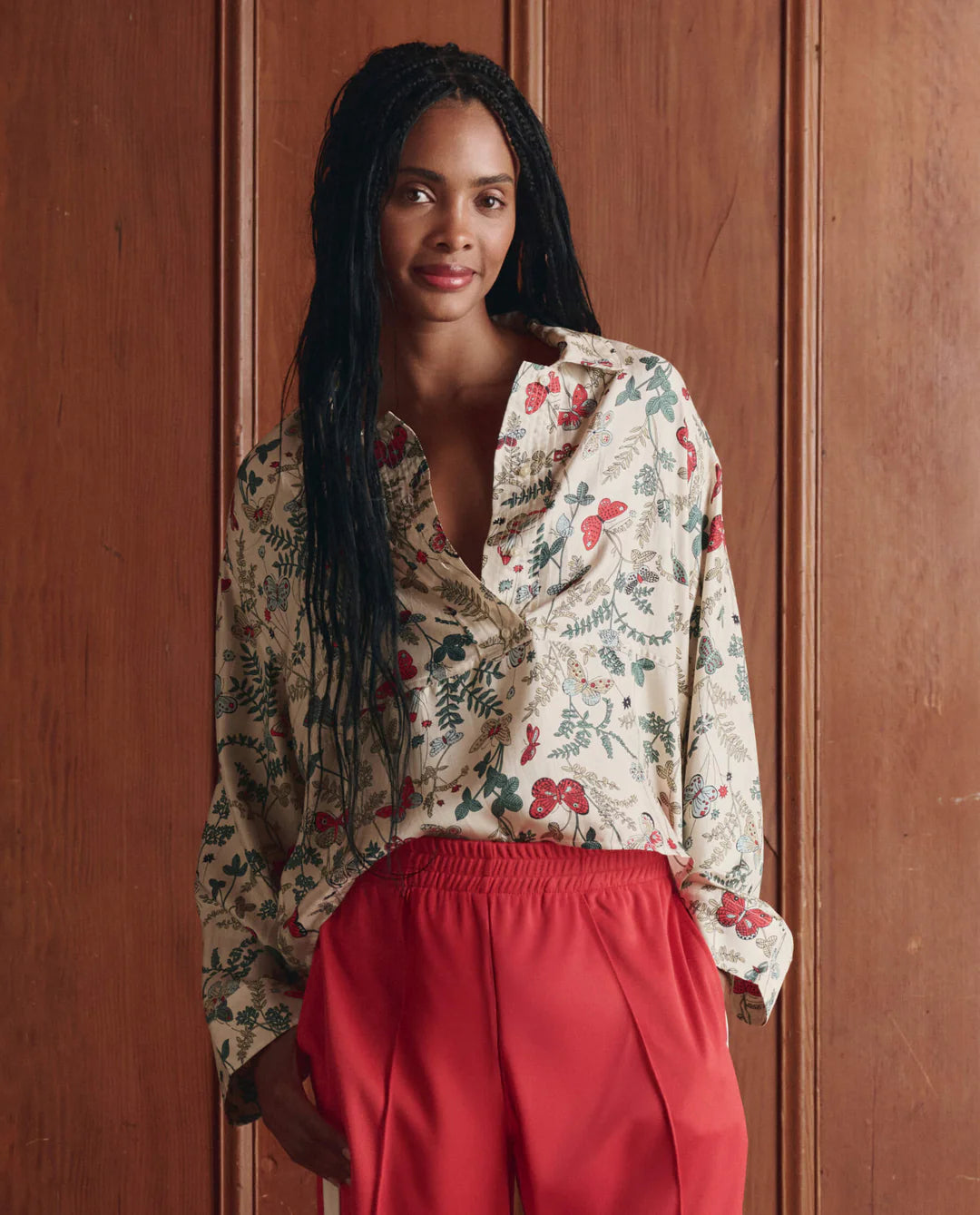 Woman wearing a floral blouse and red pants against a wooden background
