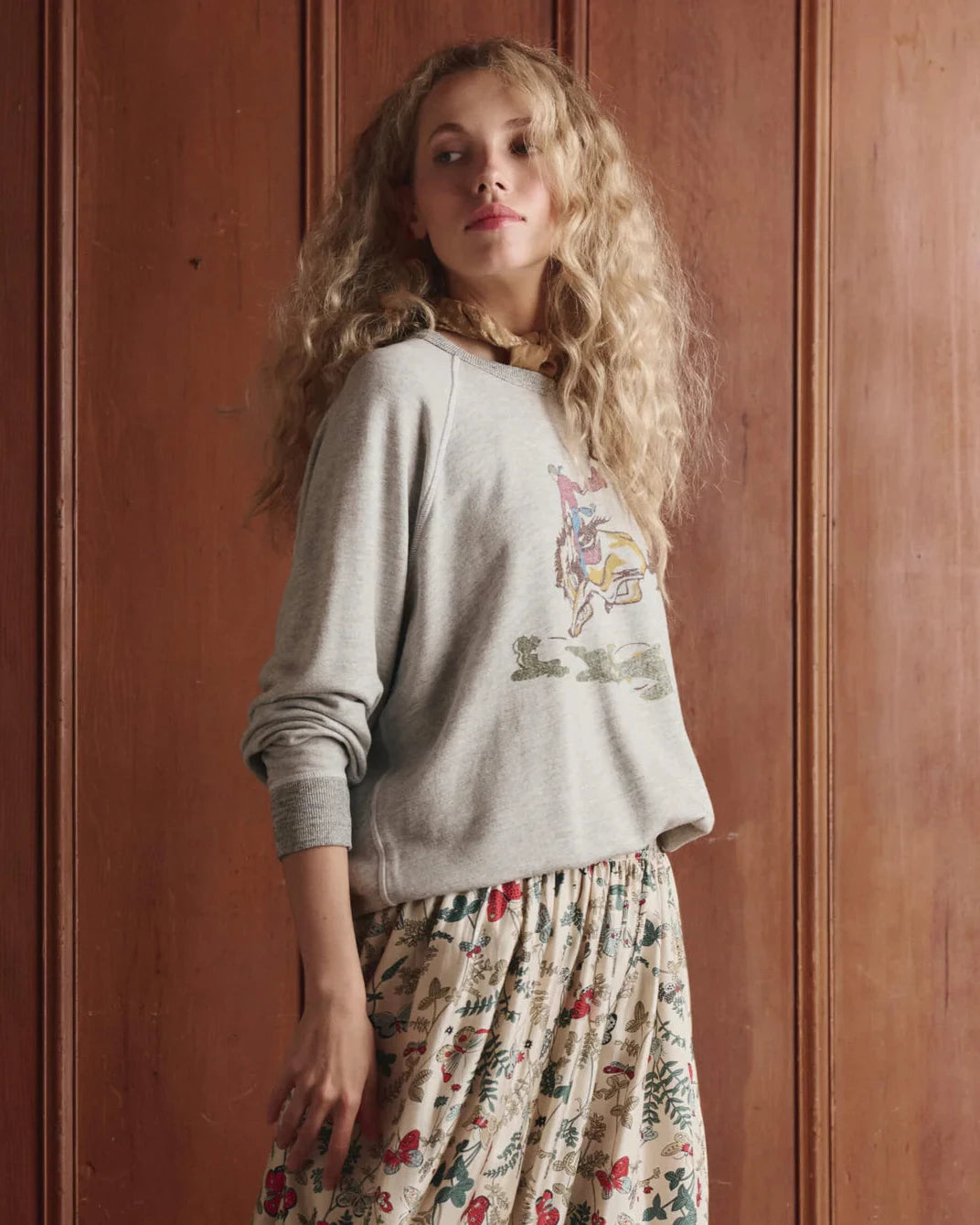 Woman wearing a gray sweatshirt with a colorful graphic design against a wooden panel background