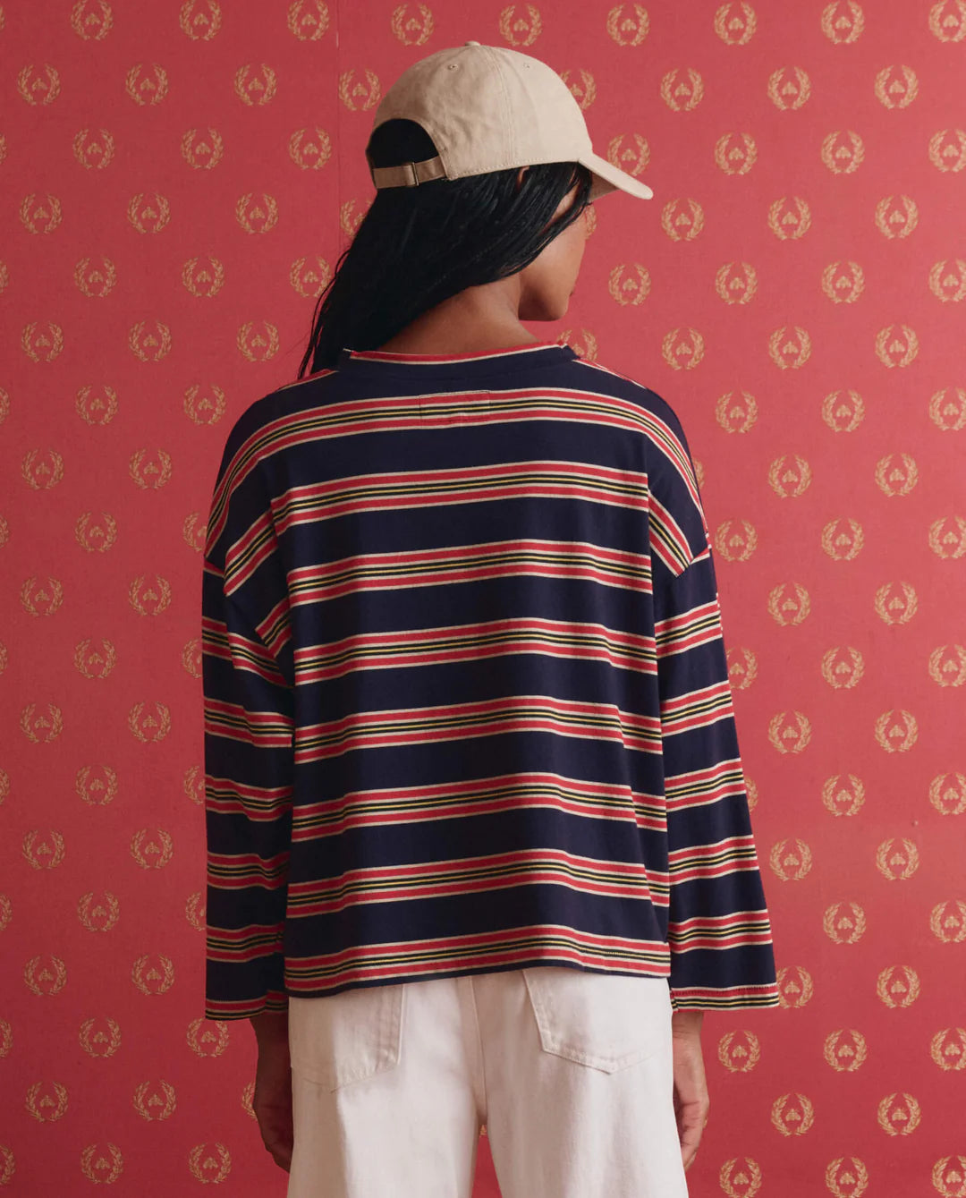 Person wearing a striped long-sleeve shirt and cap against a red patterned wall.