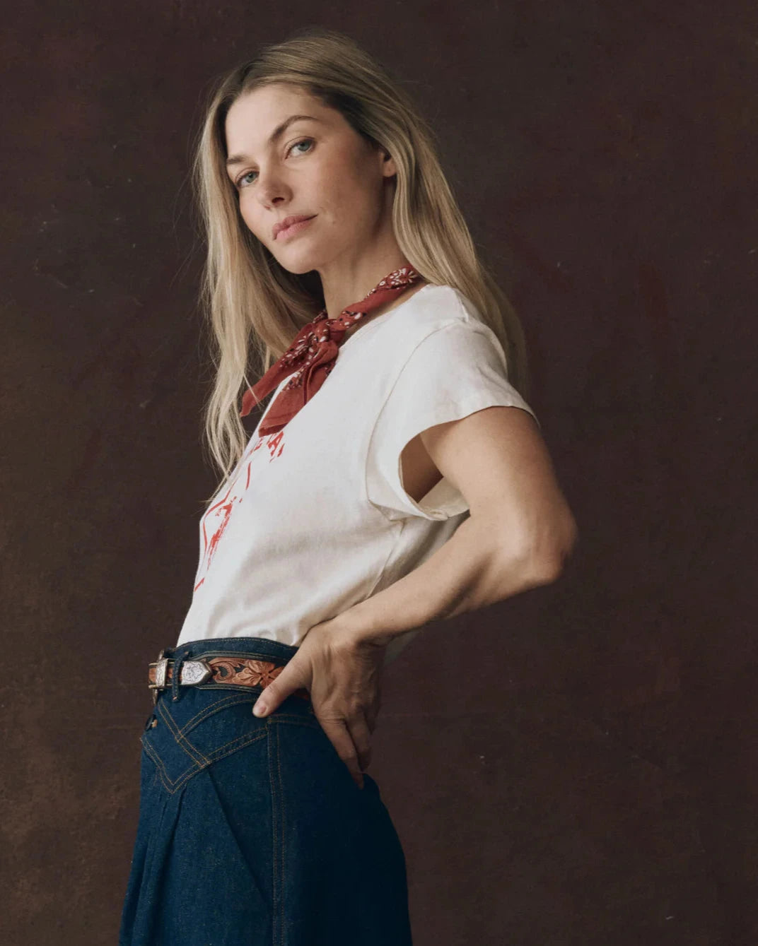 Woman wearing a white t-shirt with red design, blue jeans, and a red scarf on a dark background
