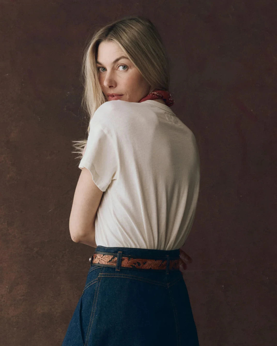 Woman wearing a white shirt and blue jeans with a brown background