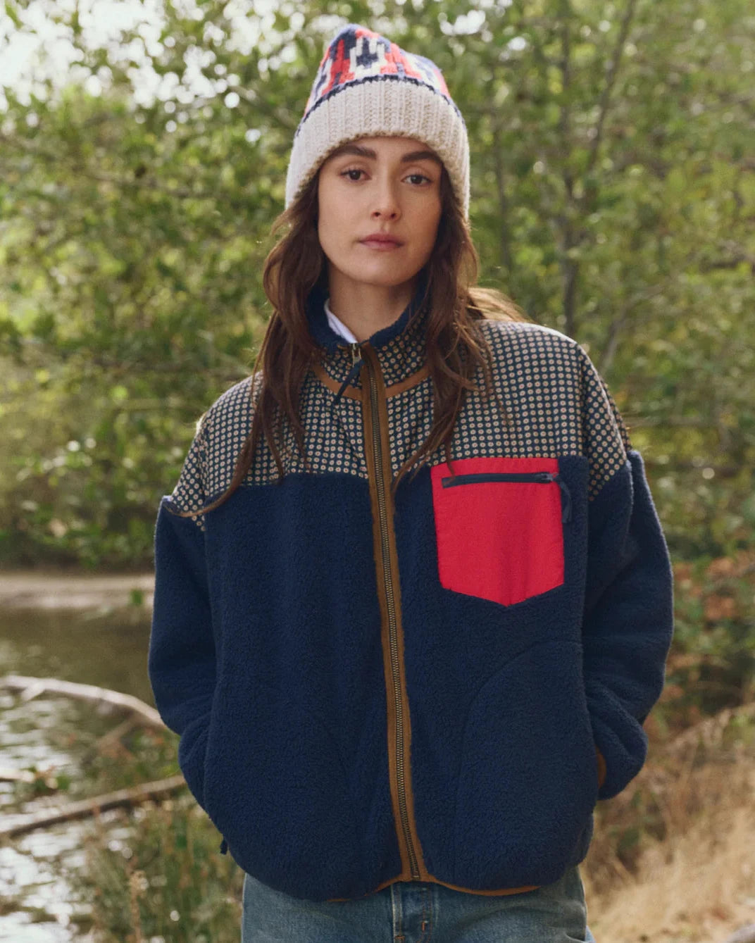Person wearing a checkered jacket with a red pocket and patterned beanie outdoors.
