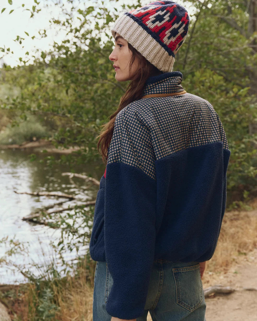 Person wearing a patterned beanie and a checkered jacket by a lake