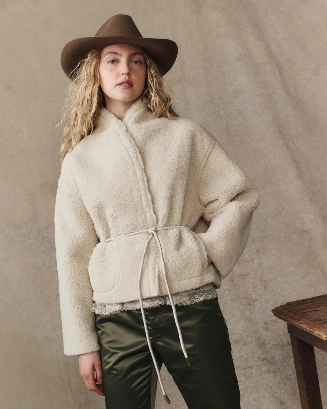Woman wearing a cream-colored fleece jacket and brown hat against a beige background